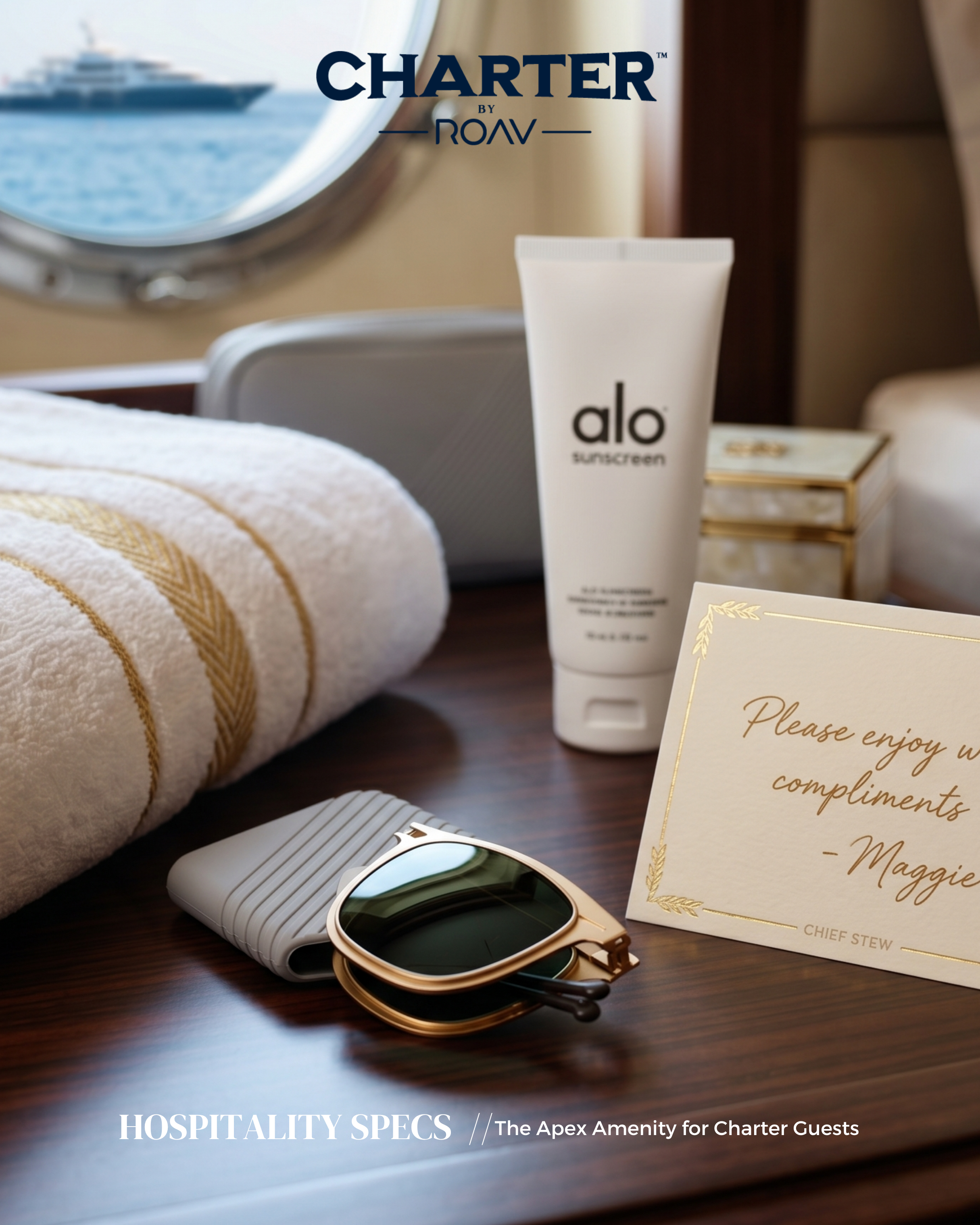 A close-up of luxury items on a wooden surface, including a white towel with gold trim, a pair of sunglasses, a white tube of Alo sunscreen, a gold-framed card with a message, and a small table with gold accents. In the background, a porthole shows a