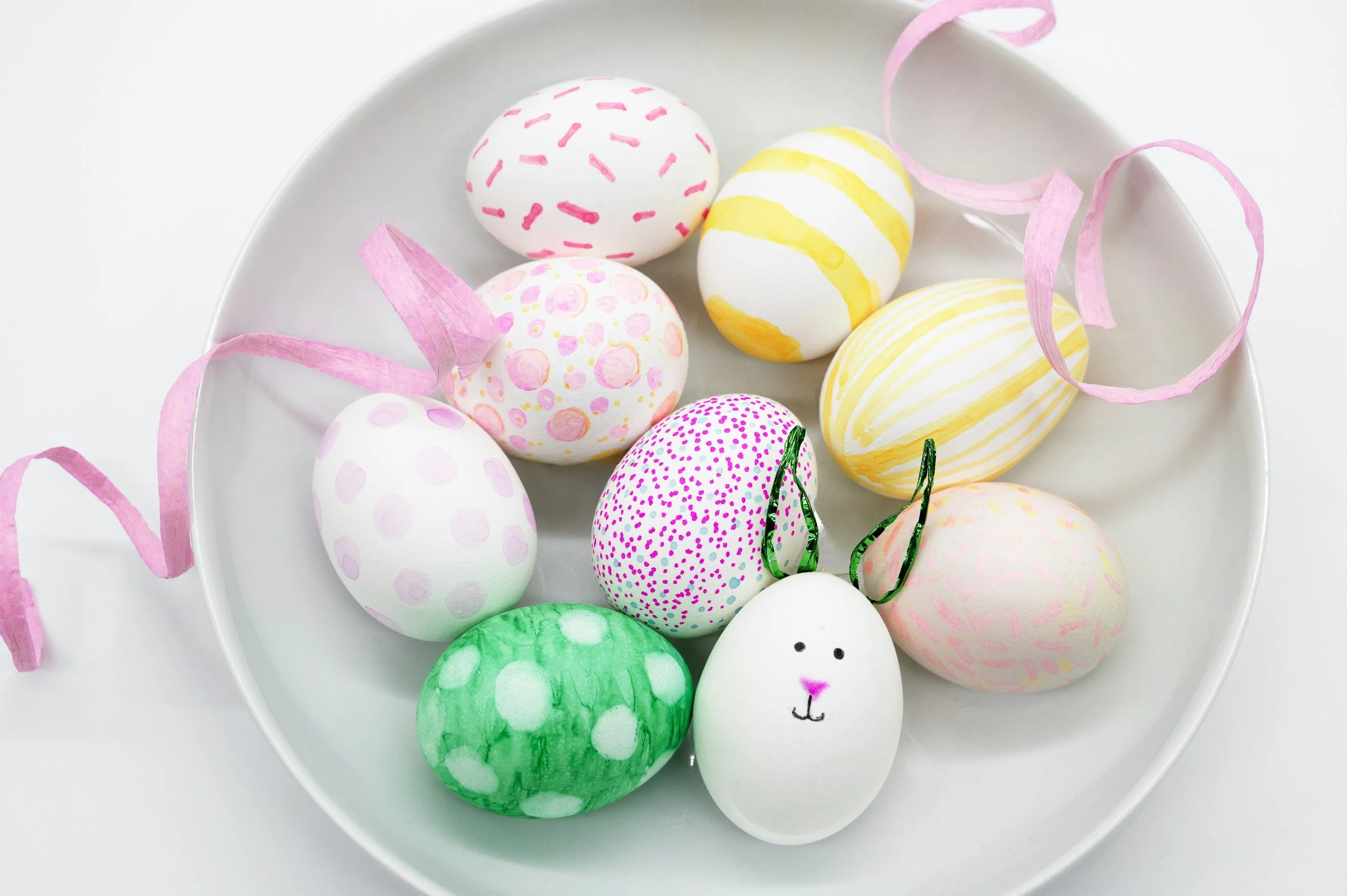 Colorful decorated Easter eggs with pink ribbons on a white plate.