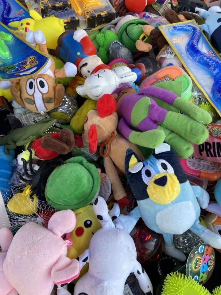 A pile of various colorful plush toys, including Pikachu, a green plush frog, a Scooby-Doo, a clown fish, and others in different shapes and sizes.