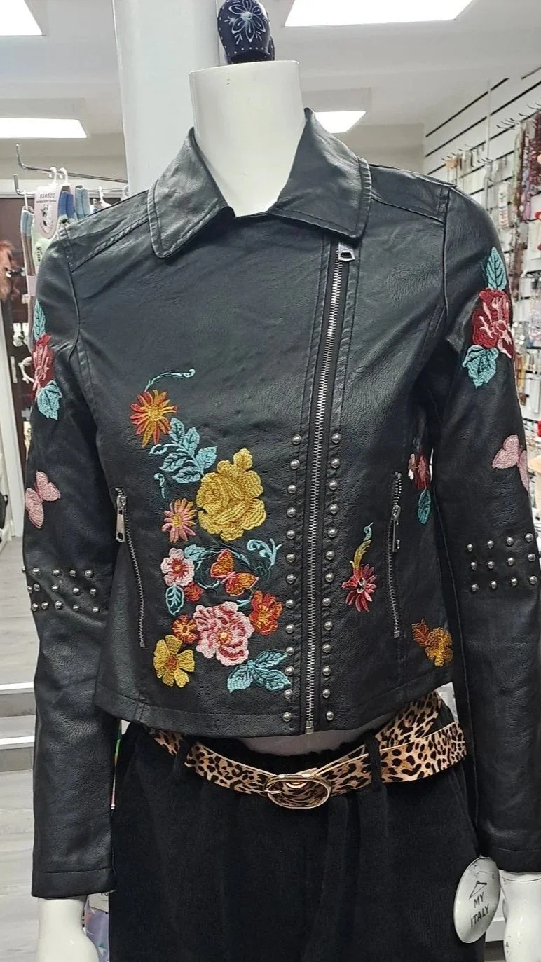 Black leather jacket with colorful floral embroidery and silver studs on a white mannequin in a store.