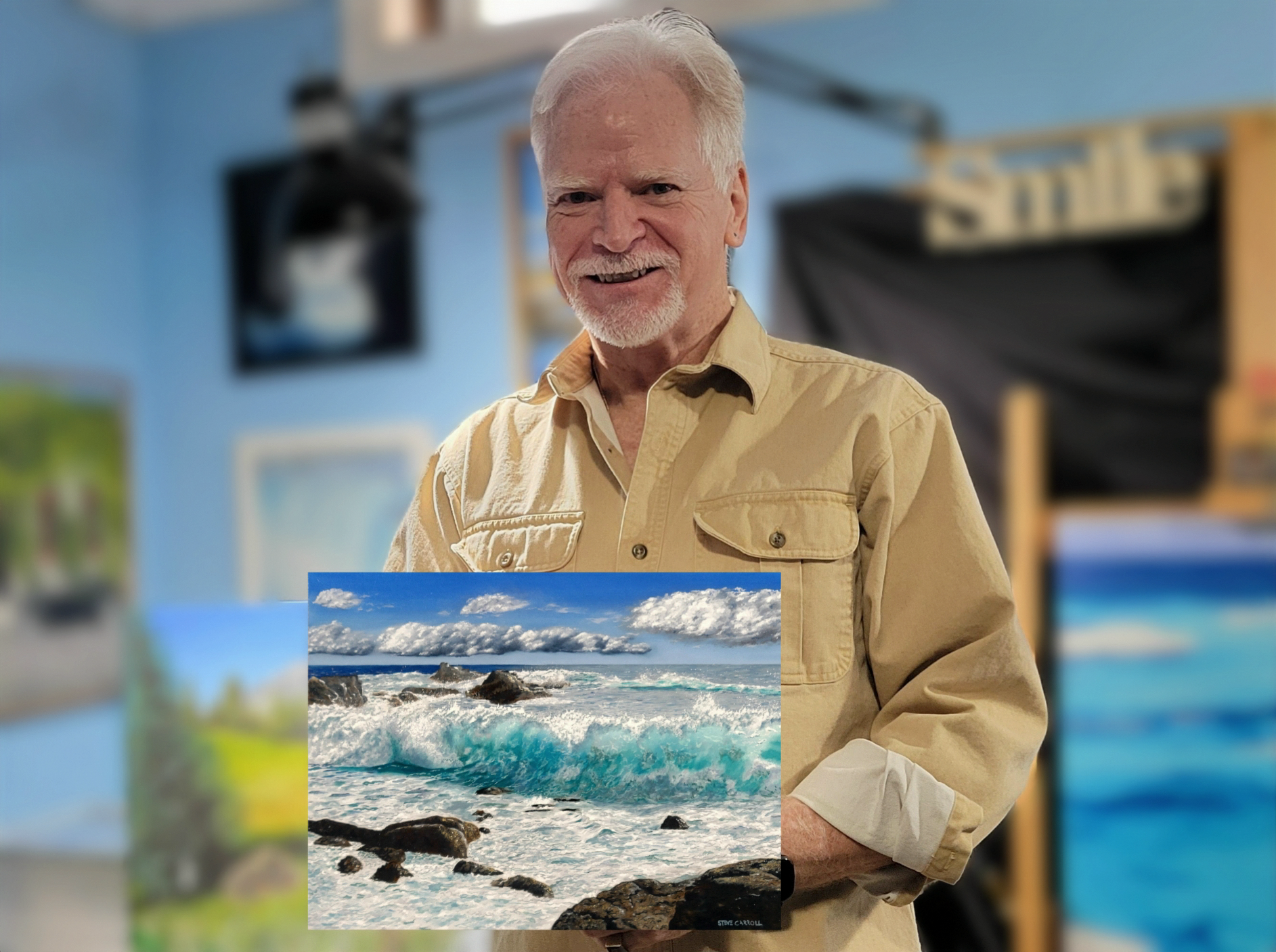 Artist Steve Carroll smiling, wearing a beige button-up shirt, standing in his art studio holding his oil painting named Teal I Sea You Again.