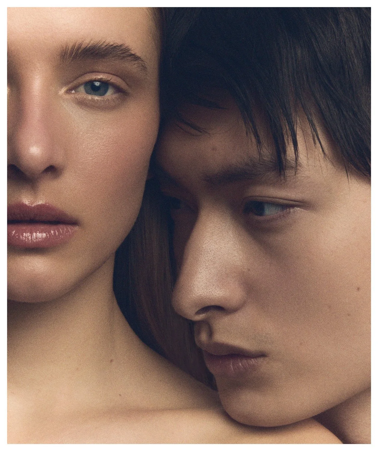 Close-up photo of two young women, one with fair skin and blue eyes and the other with darker skin, dark hair, and closed lips, resting their faces closely together.