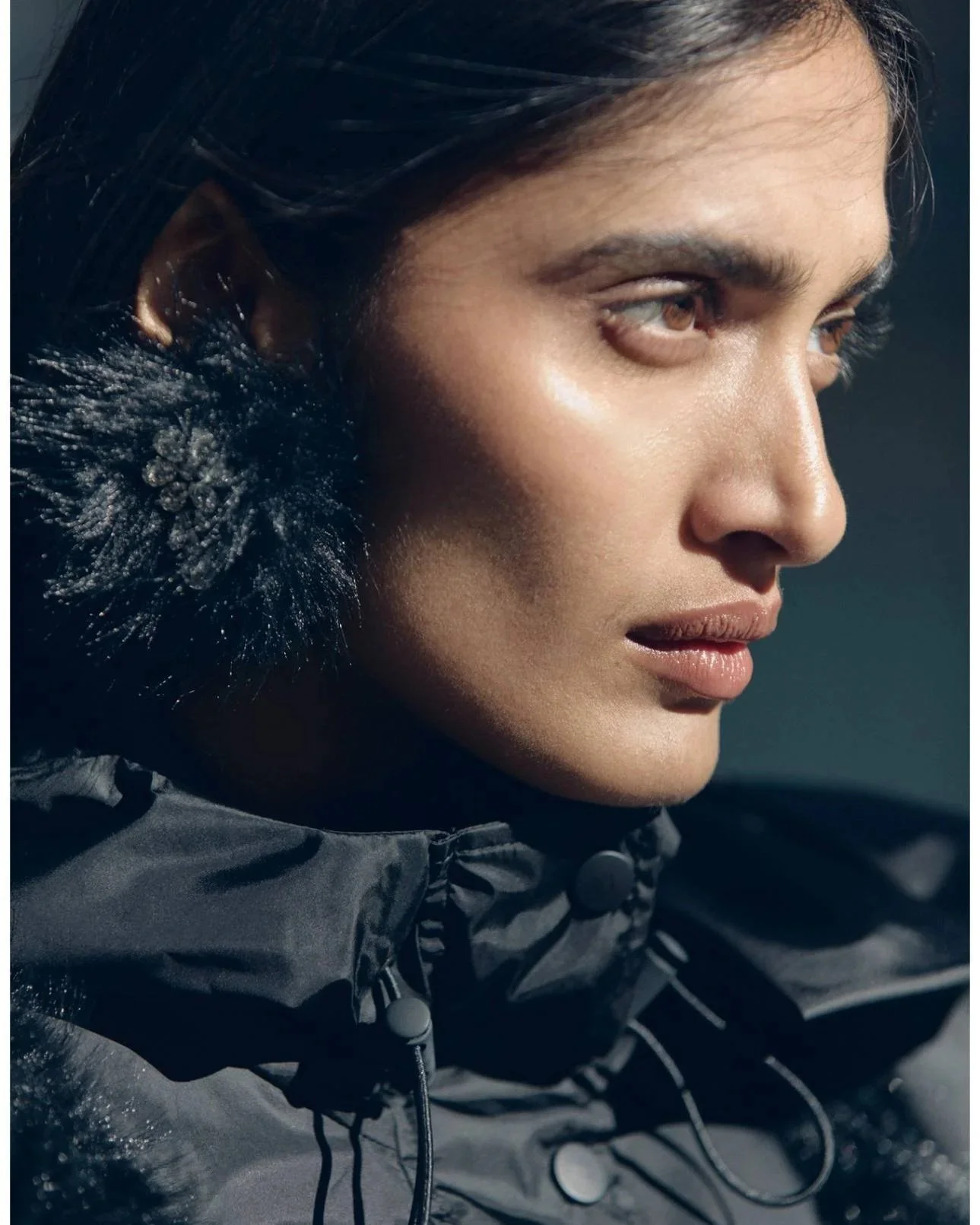 Close-up of a woman with dark hair wearing a black, water-resistant jacket with a fur-lined hood or collar.