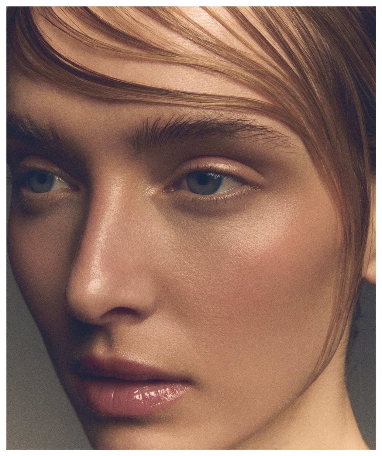 Close-up of a person's face focusing on the eye, eyebrow, nose, cheekbone, and lips with natural makeup and styled hair.