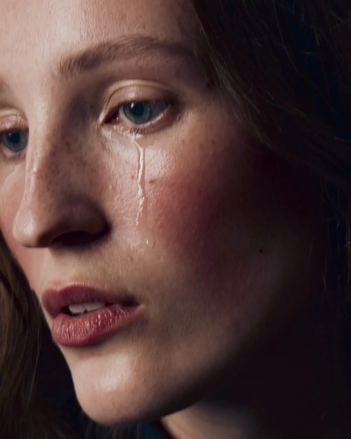 Close-up of a young woman's face with blue eyes and freckles, showing a tear rolling down her cheek.