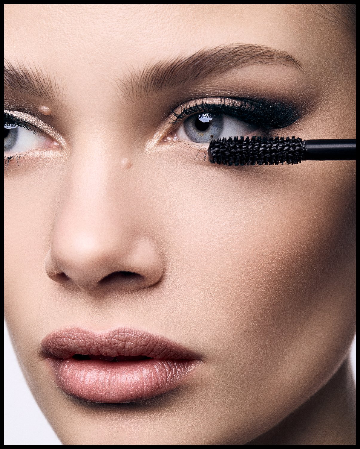 Close-up of a woman's face applying mascara to her eyelashes with a black mascara wand.