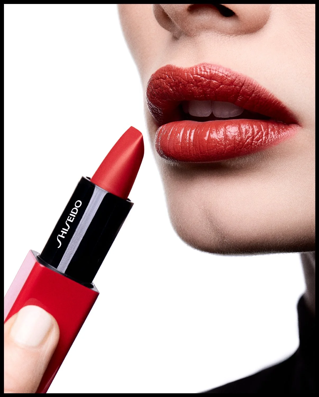 Close-up of a woman with red lipstick touching her lips with a red lipstick stick in hand, against a white background.