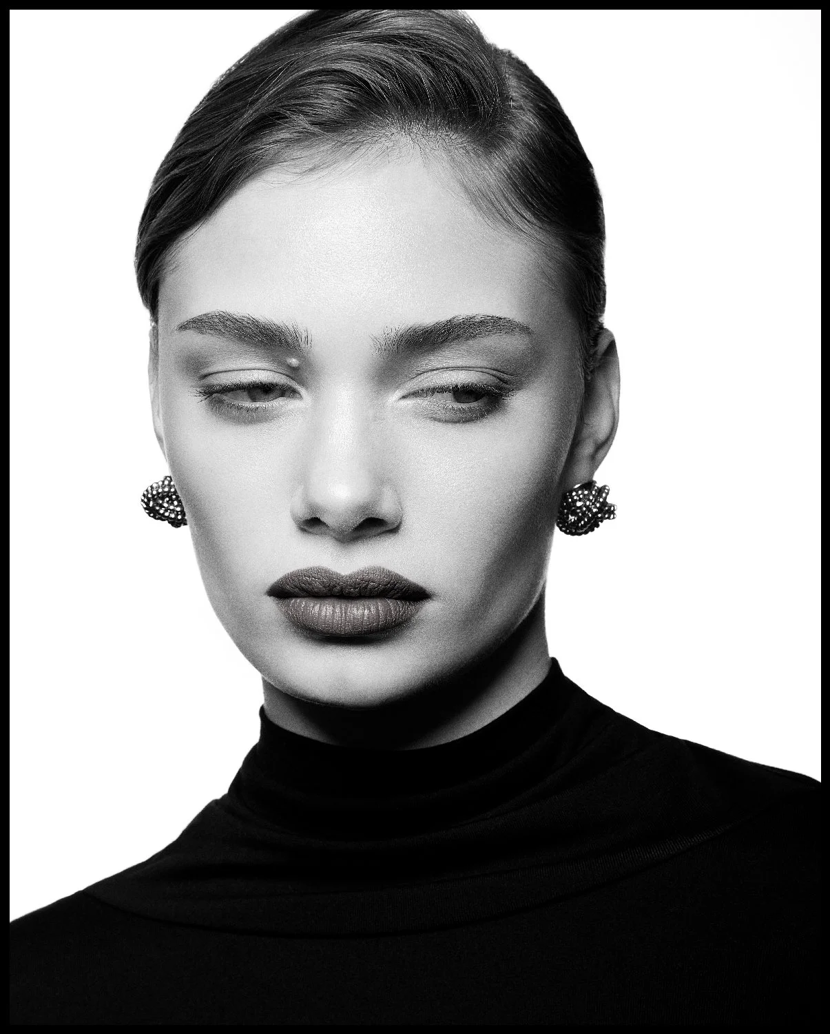 Black and white portrait of a woman with her eyes half-closed, wearing earrings and a high-neck top.
