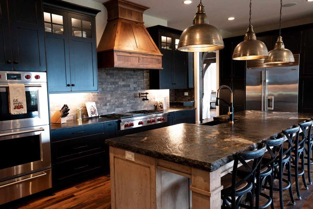 Modern kitchen with dark blue cabinets, a large granite island with seating, stainless steel appliances, and pendant lighting.