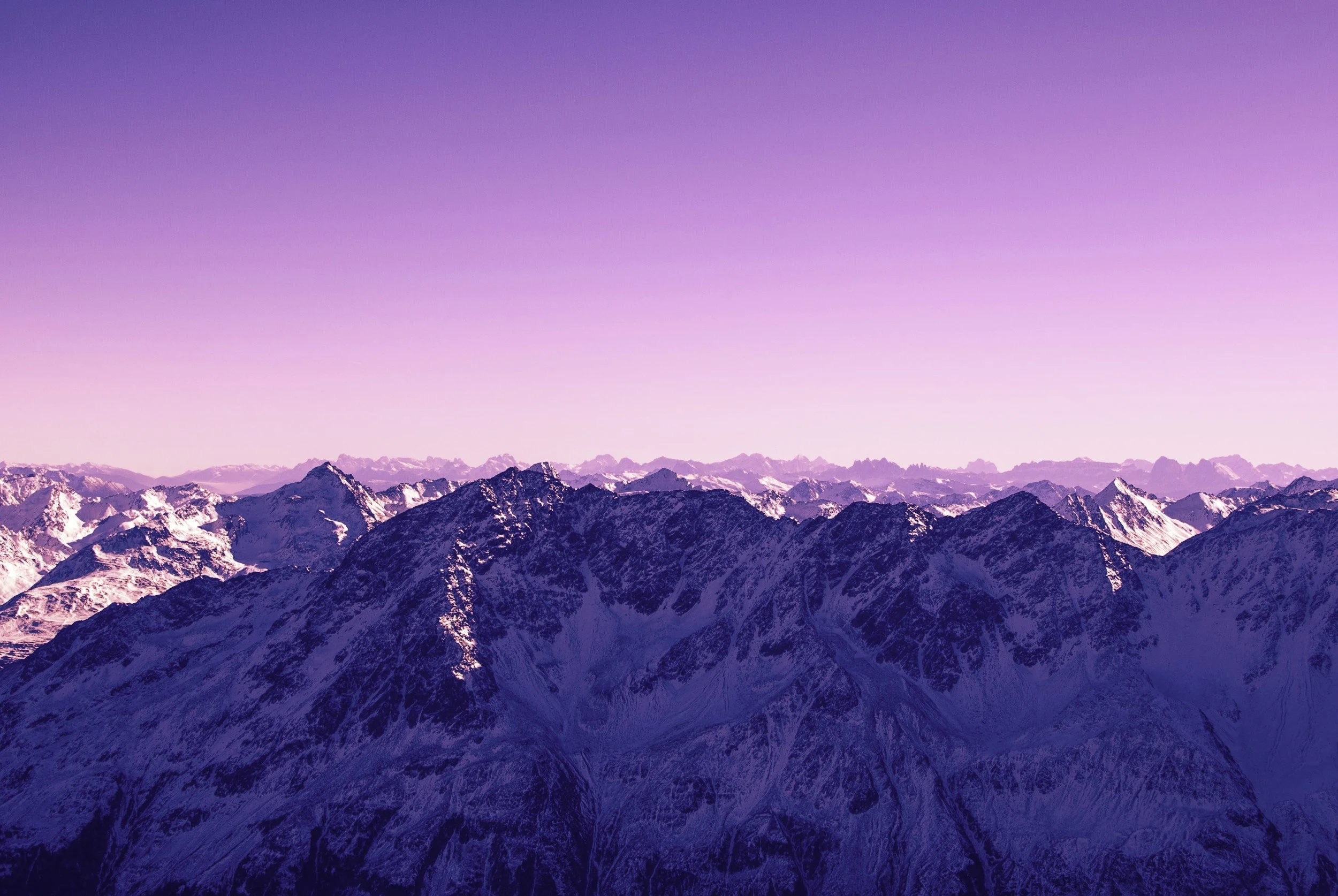 Snow-covered mountain range under a pastel pink and purple sky.