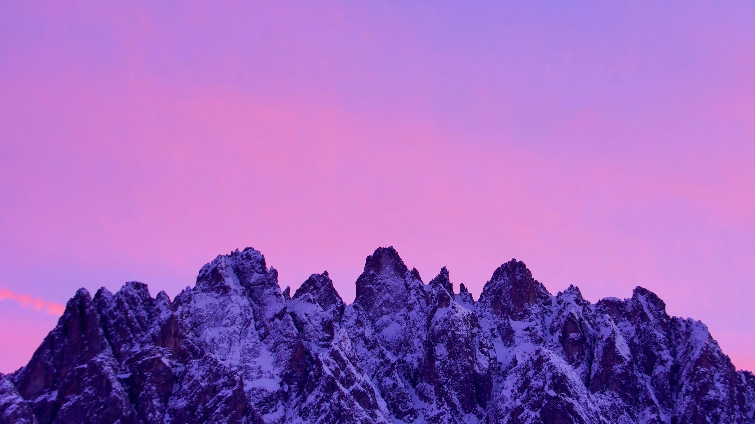 Snow-capped mountain peaks at dusk with a pink and purple sky.