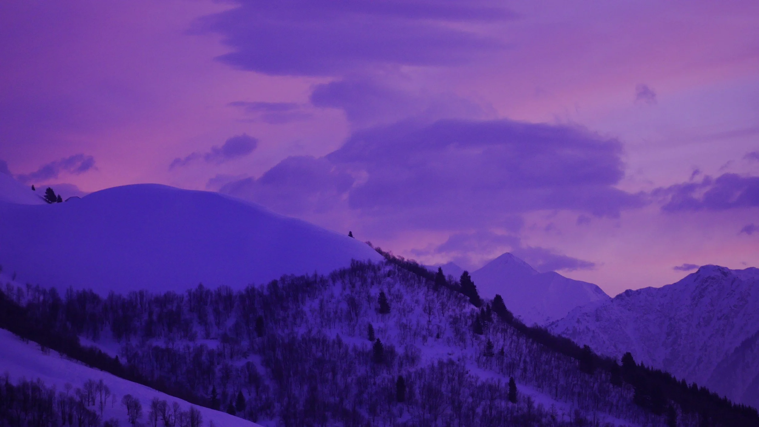 Snow-covered mountains under a purple-tinted sky with clouds and distant peaks.