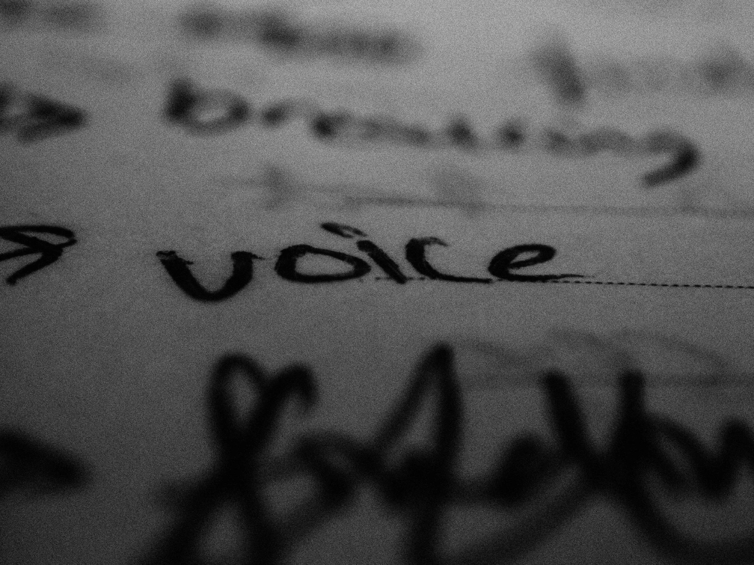 Close-up of handwritten words "voice" and other words on paper in black and white.