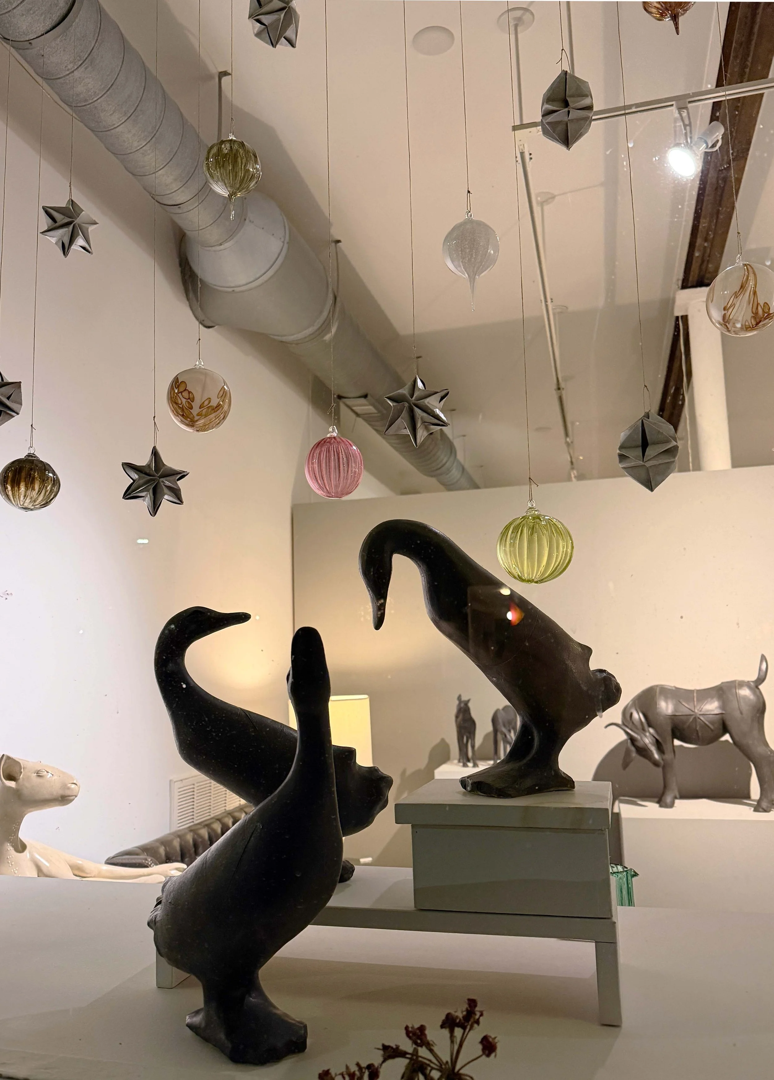 Decorative black sculpture of a stylized animals, ducks with abstract shapes, displayed on a table in a room with hanging glass ornaments and animal statues in the background.