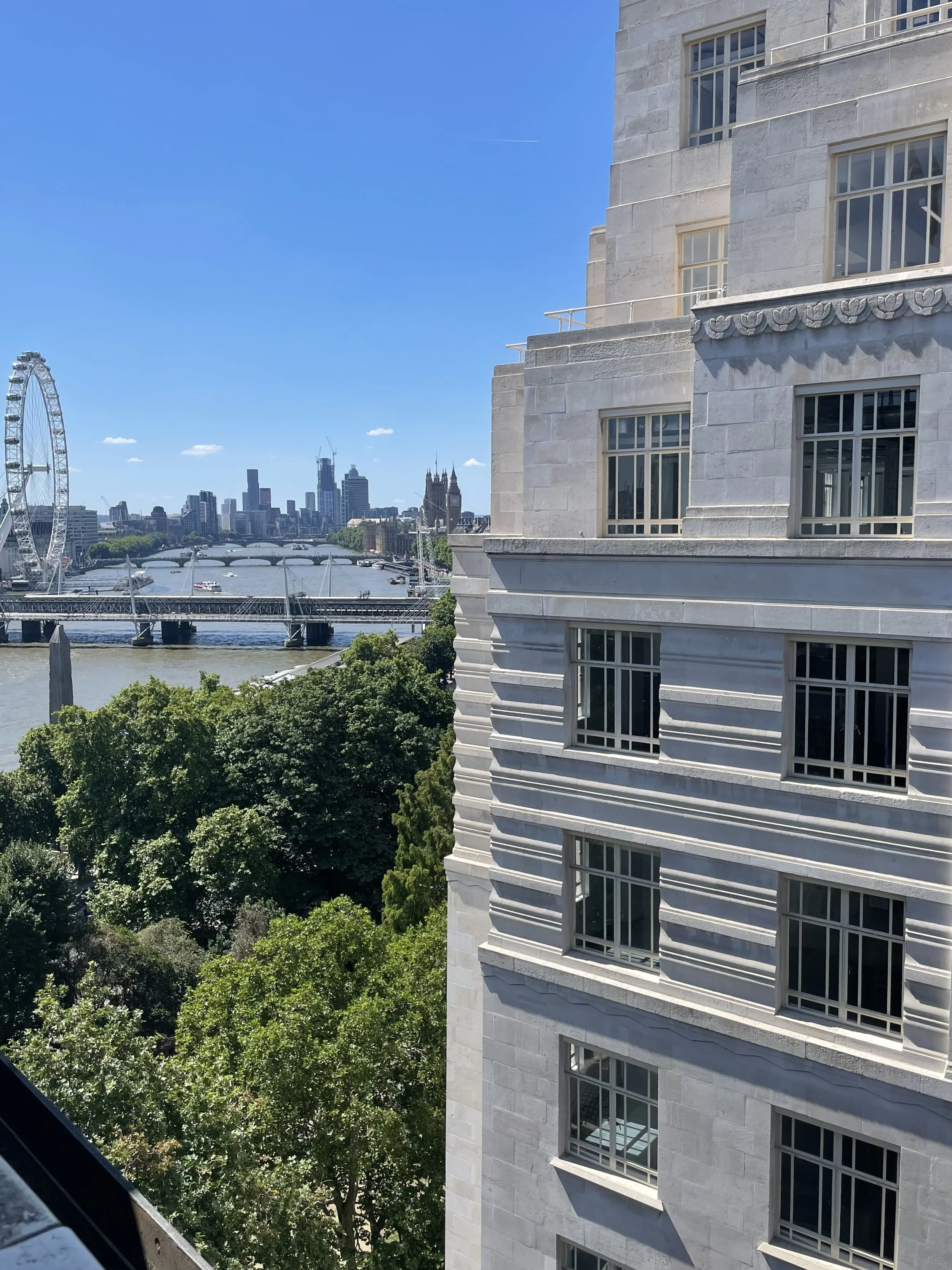 Image is the view from a room at The Savoy Hotel showcasing the London Eye and the River Thames on a sunny day