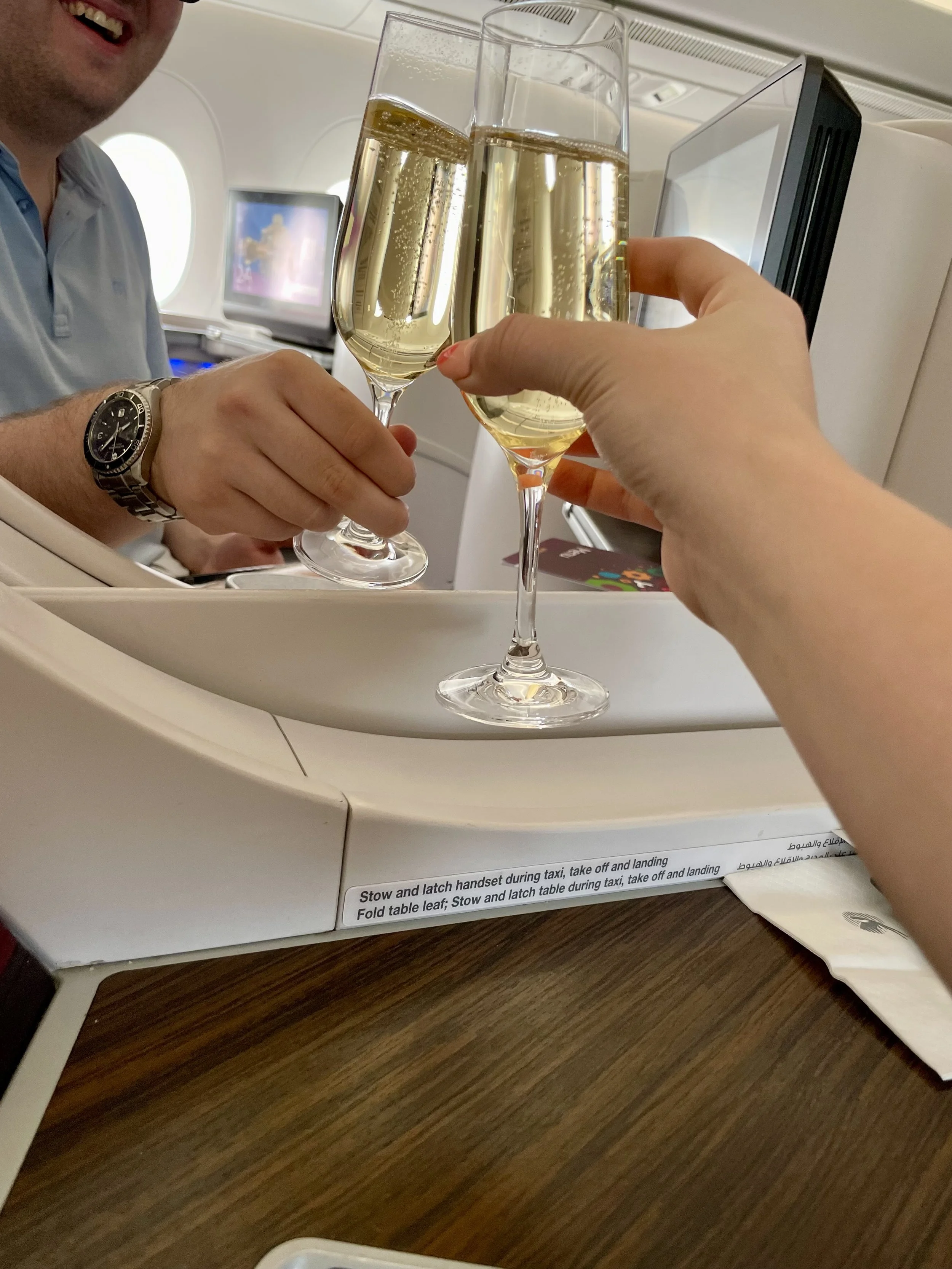 Photo shows a couple doing a toast with two champagne glasses in the business class cabin of a Qatar Airways airplane