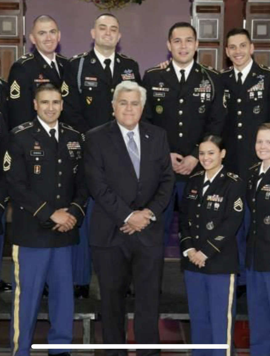 Group photo of eight uniformed military personnel and one man in a suit, standing indoors, smiling for the camera.
