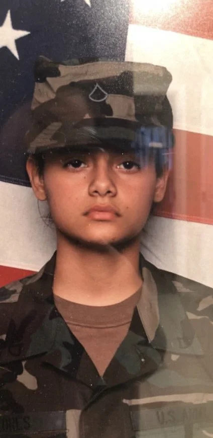 A young person in military uniform standing in front of an American flag.