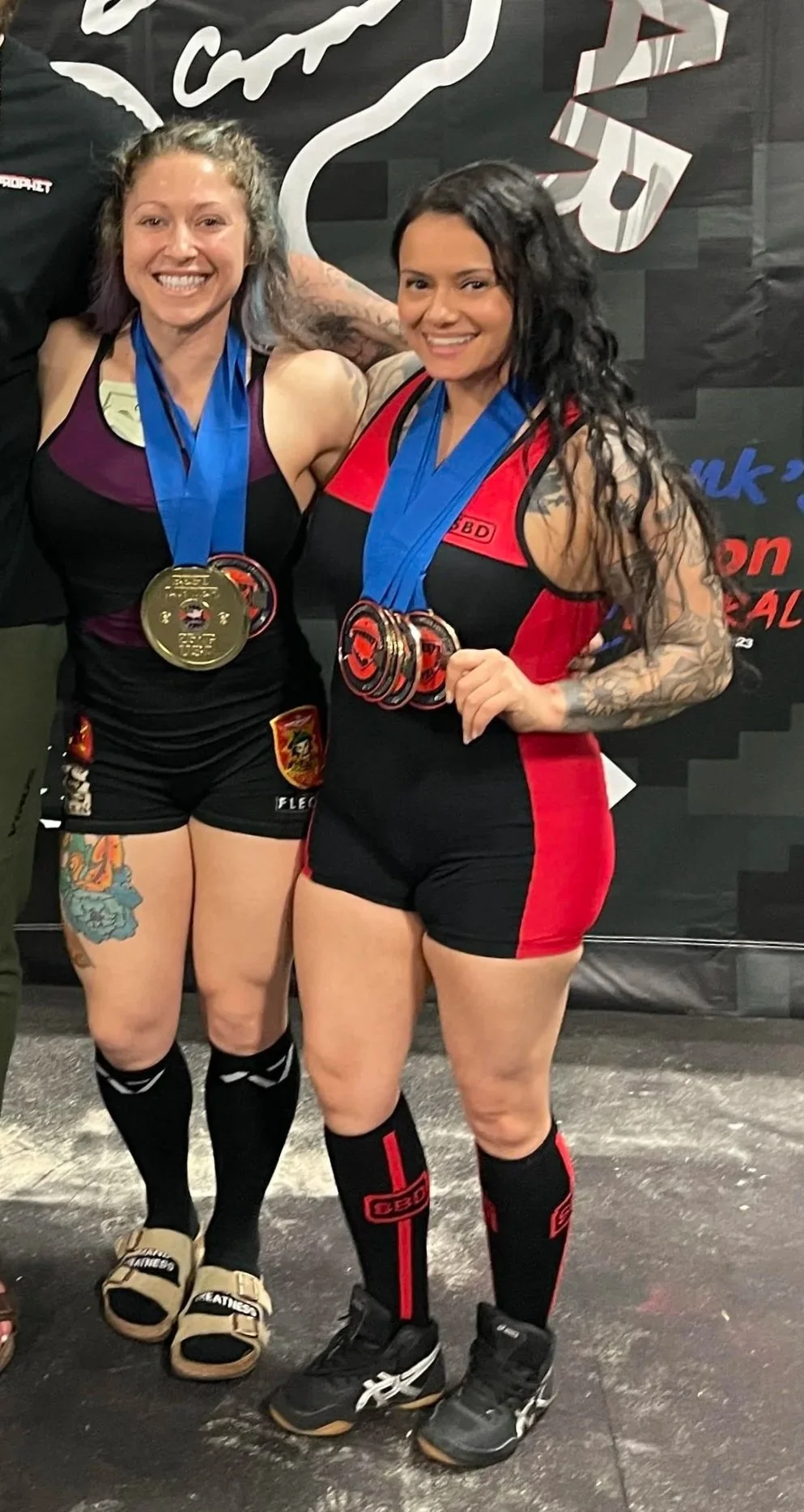 Two women wearing athletic gear with medals around their necks, standing together, smiling after a competition.