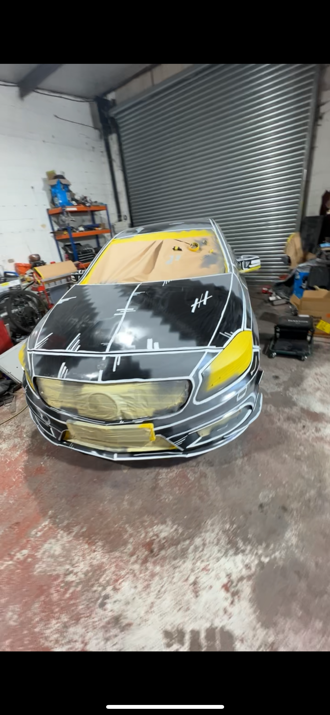 A car in a workshop with masking tape and paper covering parts of it, undergoing a paint or customization process.