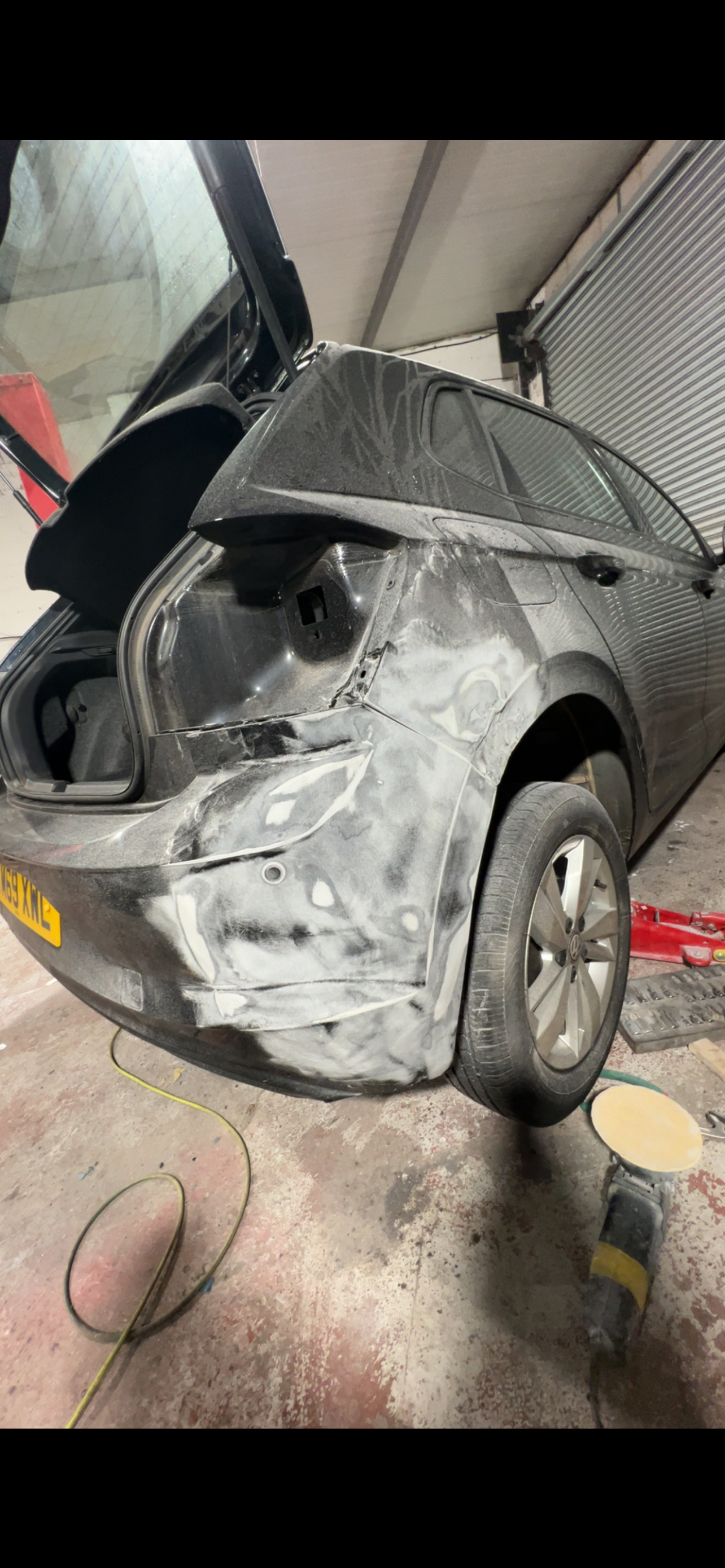 A black car with rear damage and white repair marks inside a garage.