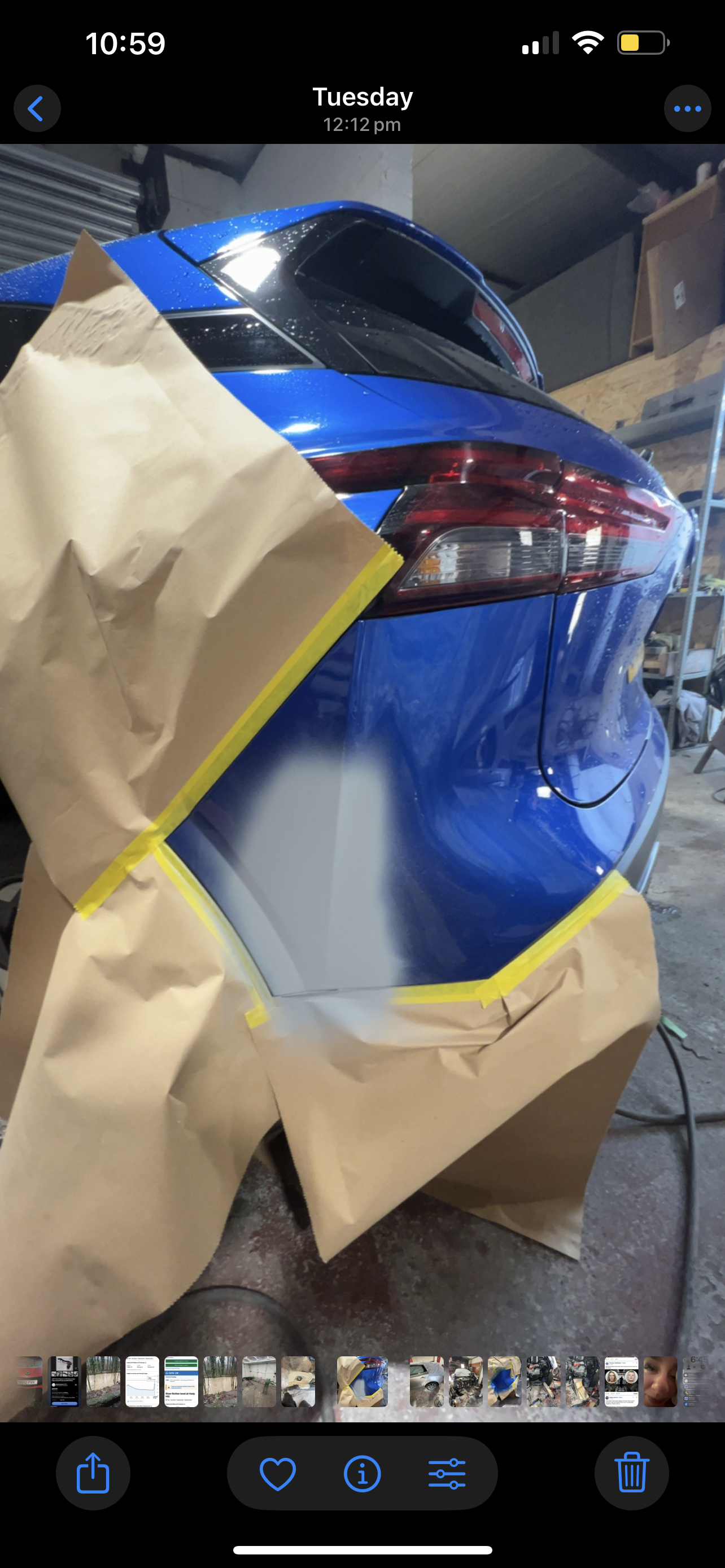 A blue car in a garage, partially masked with brown paper and yellow tape, possibly for painting or repair.