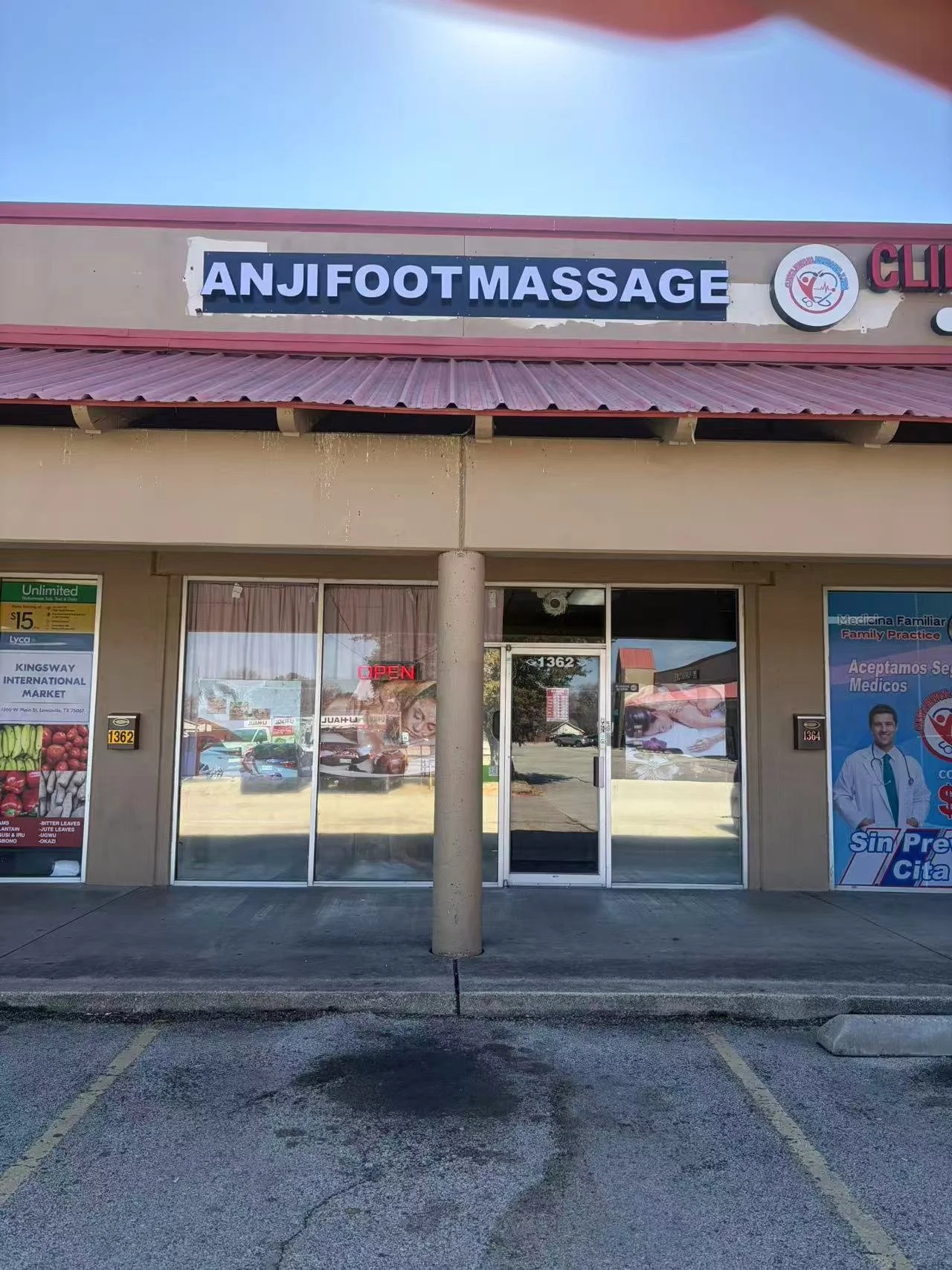 Front of a storefront labeled 'ANJI FOOT MASSAGE' with a glass door and windows, a neon 'OPEN' sign, parking spaces, and advertisements for local businesses.