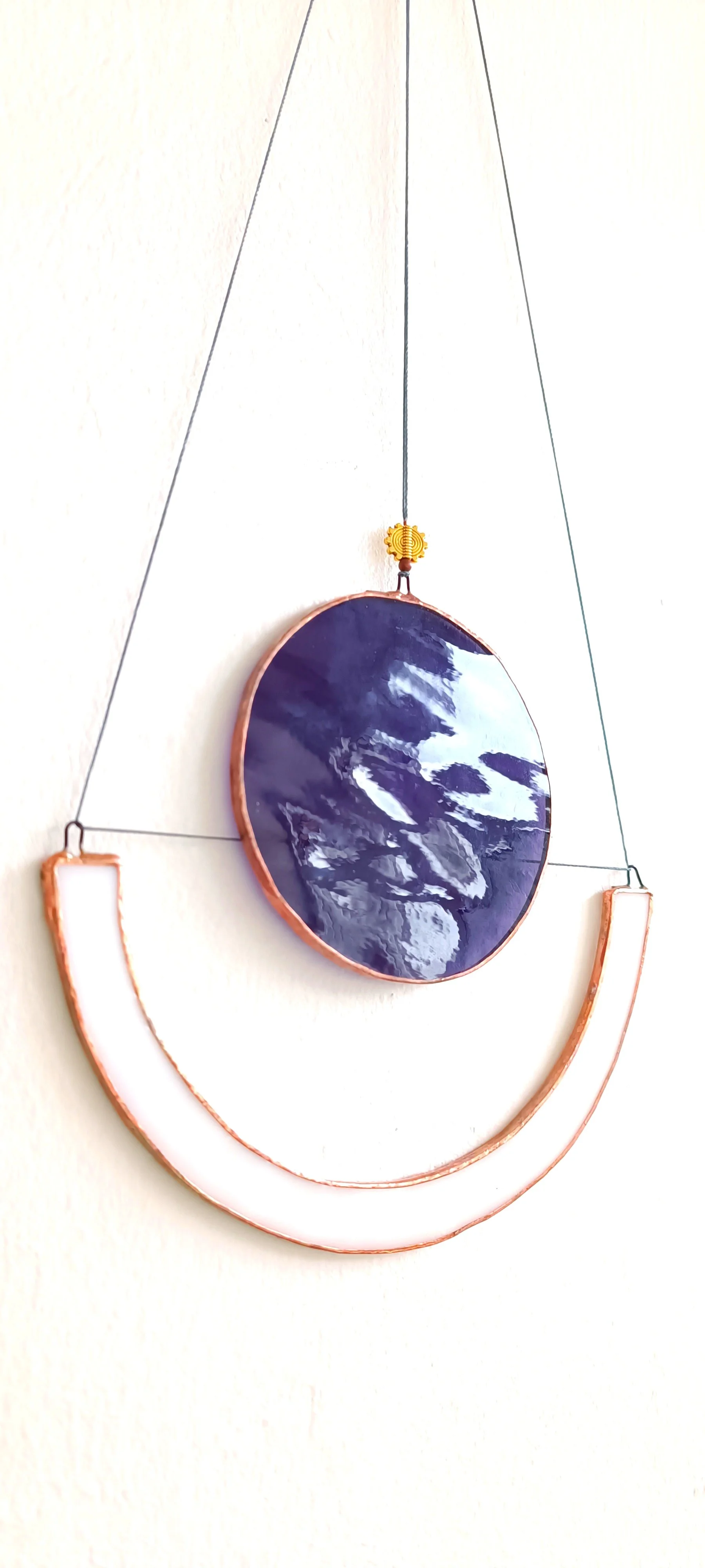 Décoration murale avec un disque en céramique bleu entouré de fil métallique, suspendu par des fils noirs avec une petite pièce en forme de soleil doré en haut. Suspension unique en vitrail. Création unique crée par Diane FRANK de l'atelier ' Le Vitr