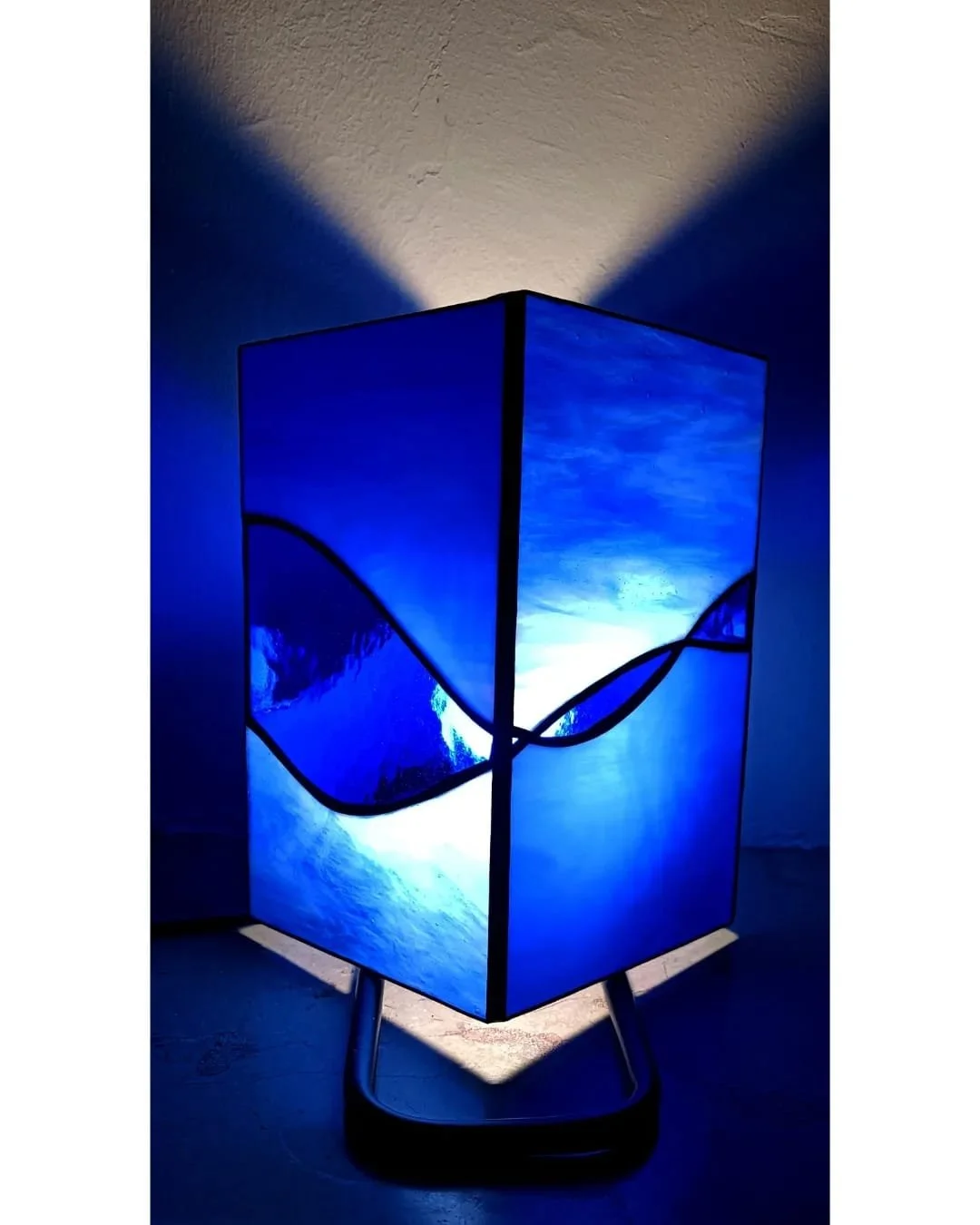 Lampe de table en vitrail créée lors d'un atelier créatif à Lille. avec un design artistique évoquant la mer en nuances de bleu, éclairée de l'intérieur, posée sur une surface en intérieur