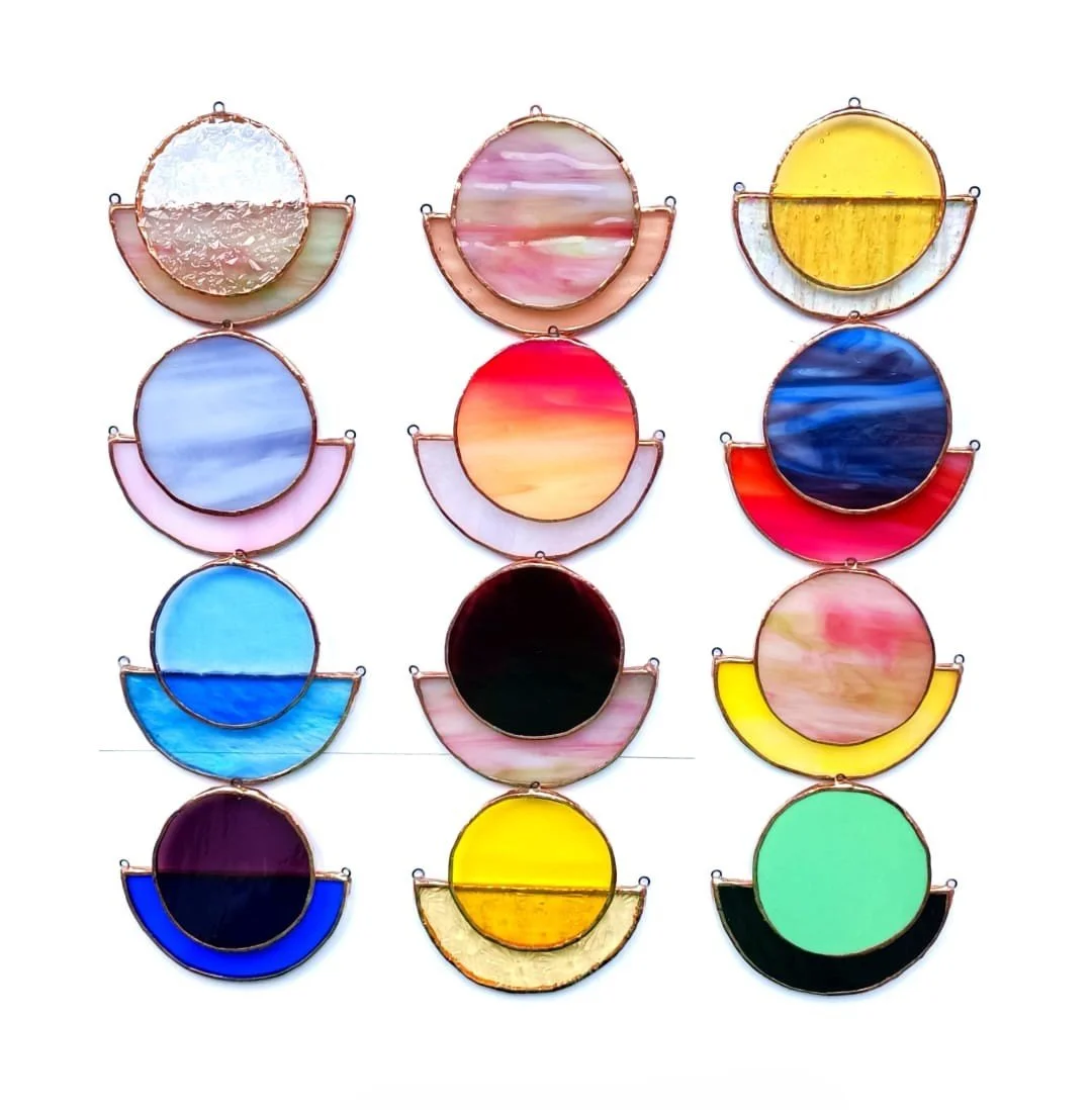 Collection de 12 pièces d'art en verre coloré, chaque pièce étant un cercle partiellement encadré en métal, disposées en trois colonnes et quatre rangées.