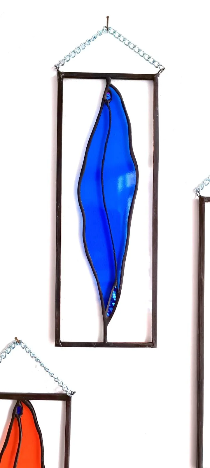 Une œuvre d'art en verre coloré bleu encadrée en métal noir, suspendue par une chaîne métallique.