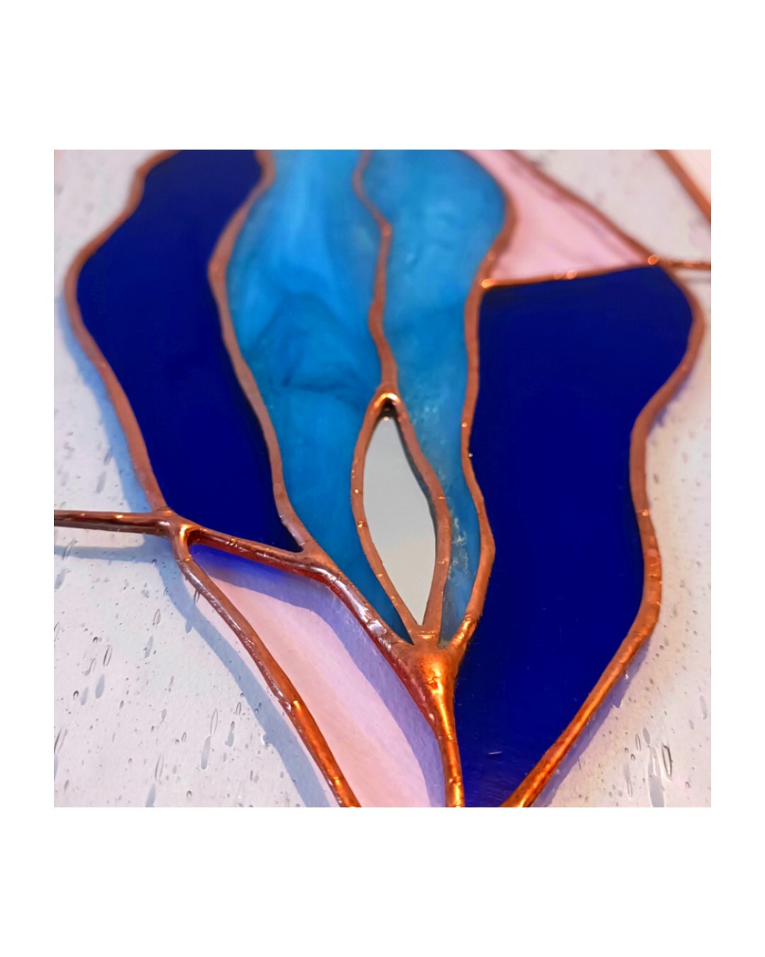 Une pièce en vitrail colorée avec des formes abstraites en bleus et roses, encadrée par des lignes en cuivre.