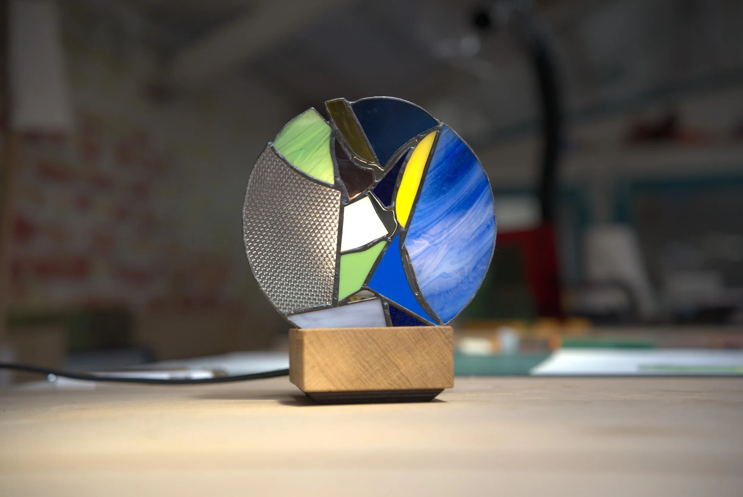 Vitrail artisanal en verre coloré avec différentes textures, posée sur une table en bois. Ce vitrail est fabriqué lors d'un atelier vitrail à Lille. Un atelier de 4h30