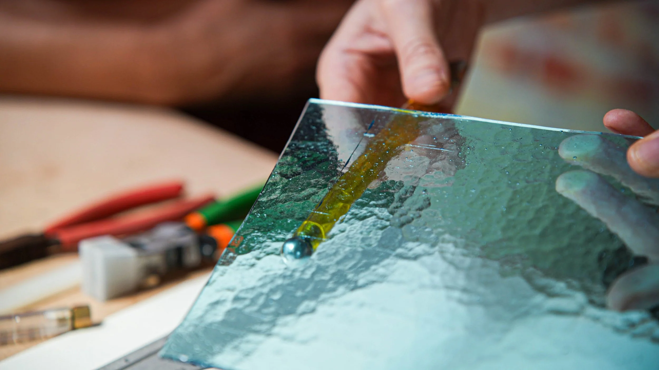 Une personne manipule une vitre en verre comme un miroir, avec des outils électriques en arrière-plan.