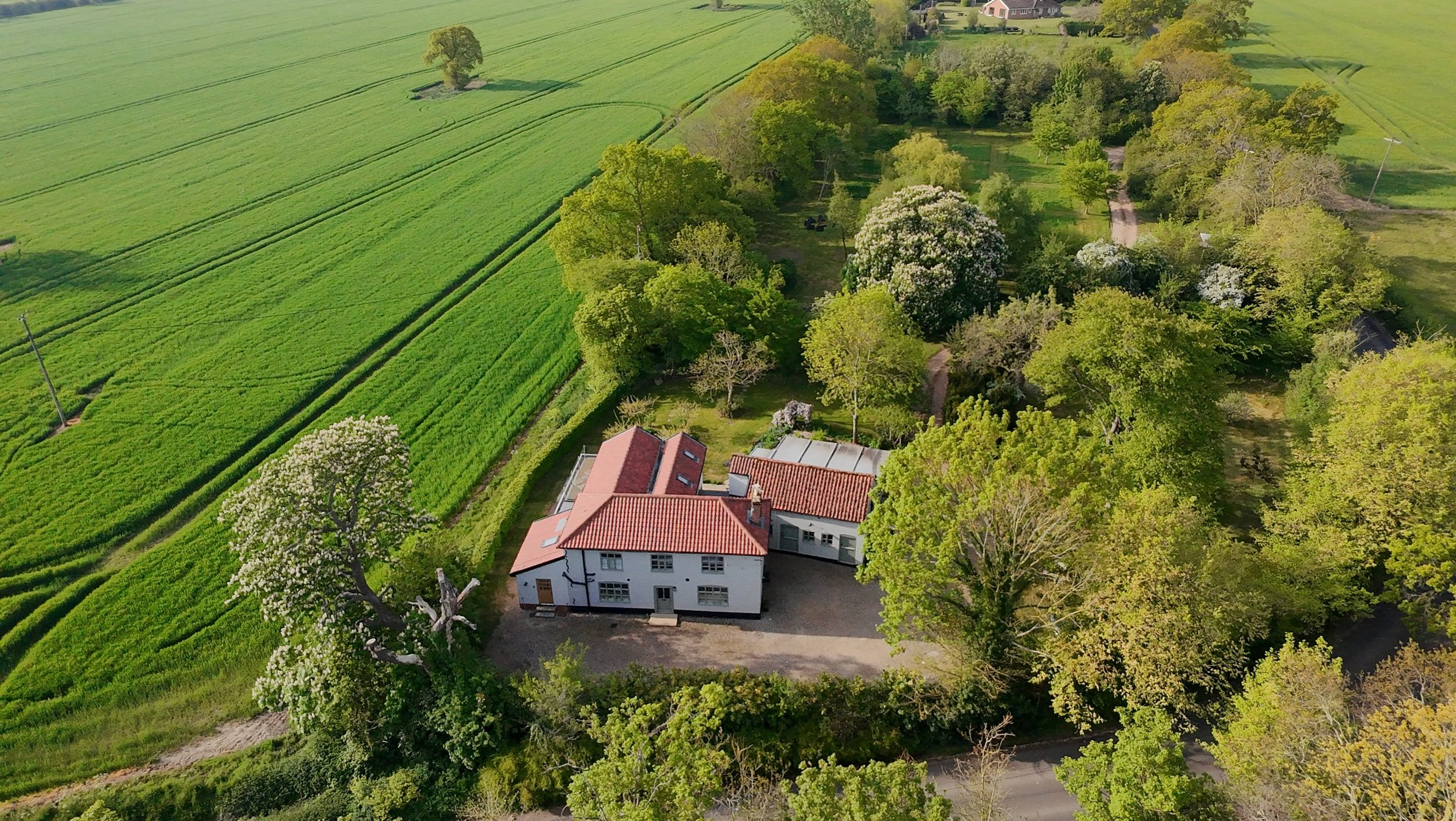 An aerial view of a house surrounded by trees and large green fields.