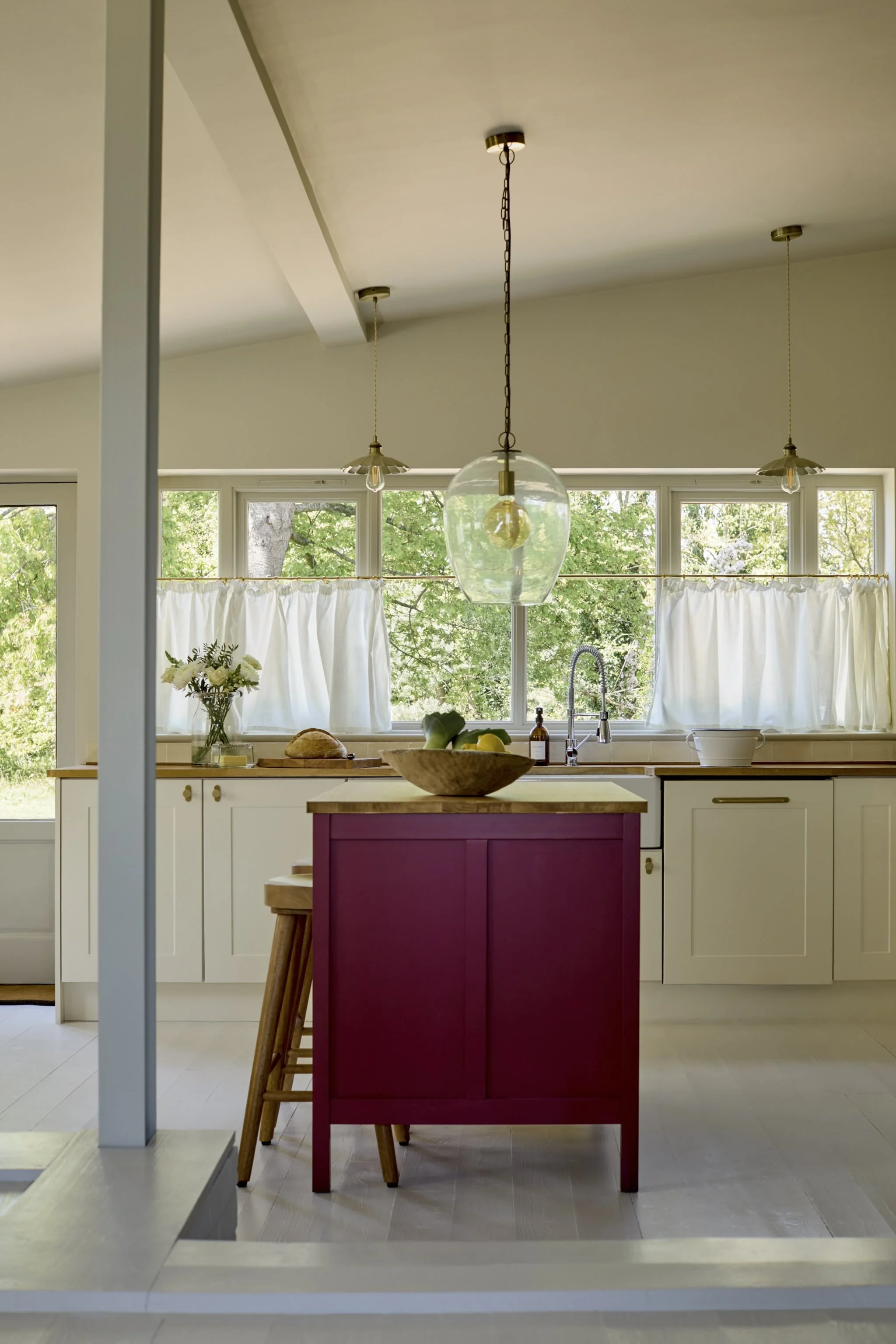 Kitchen with large window, white cabinets, a wood countertop, a small red kitchen island, a hanging glass pendant light, and greenery outside.