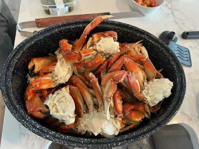 Large black container filled with cooked crab pieces with claws and shells.