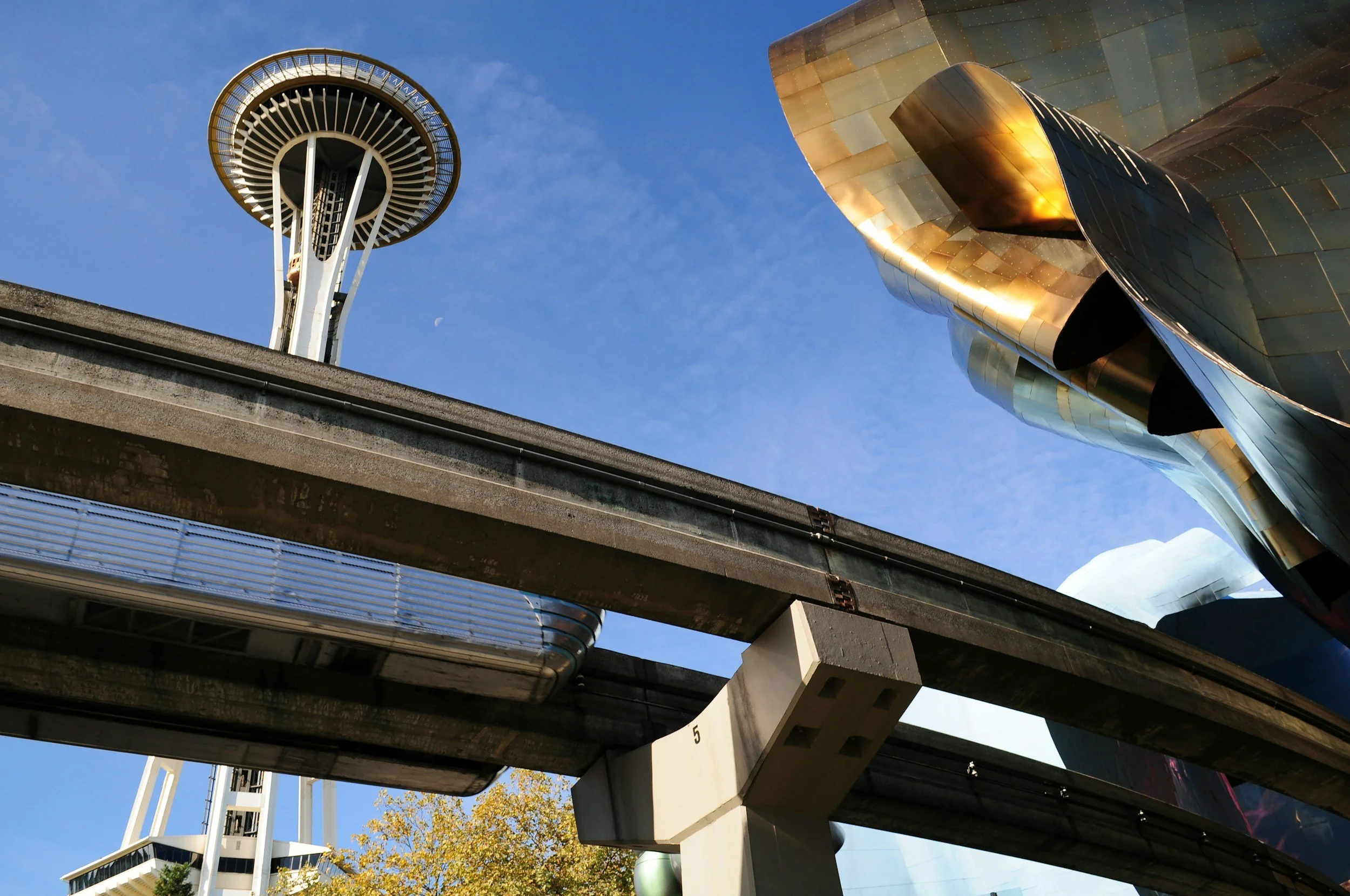 A view of the Space Needle and Chihuly Garden and Glass sculpture in Seattle, Washington, from below, with elevated train tracks in the foreground.