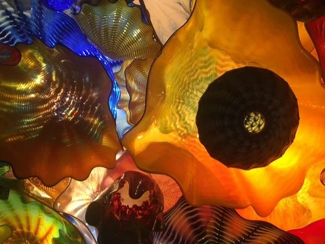 Close-up of colorful glass art pieces with textured and wavy surfaces, illuminated from behind.