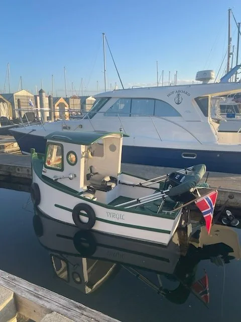 Small white and green boat named Virgili docked in marina with larger white yacht in background