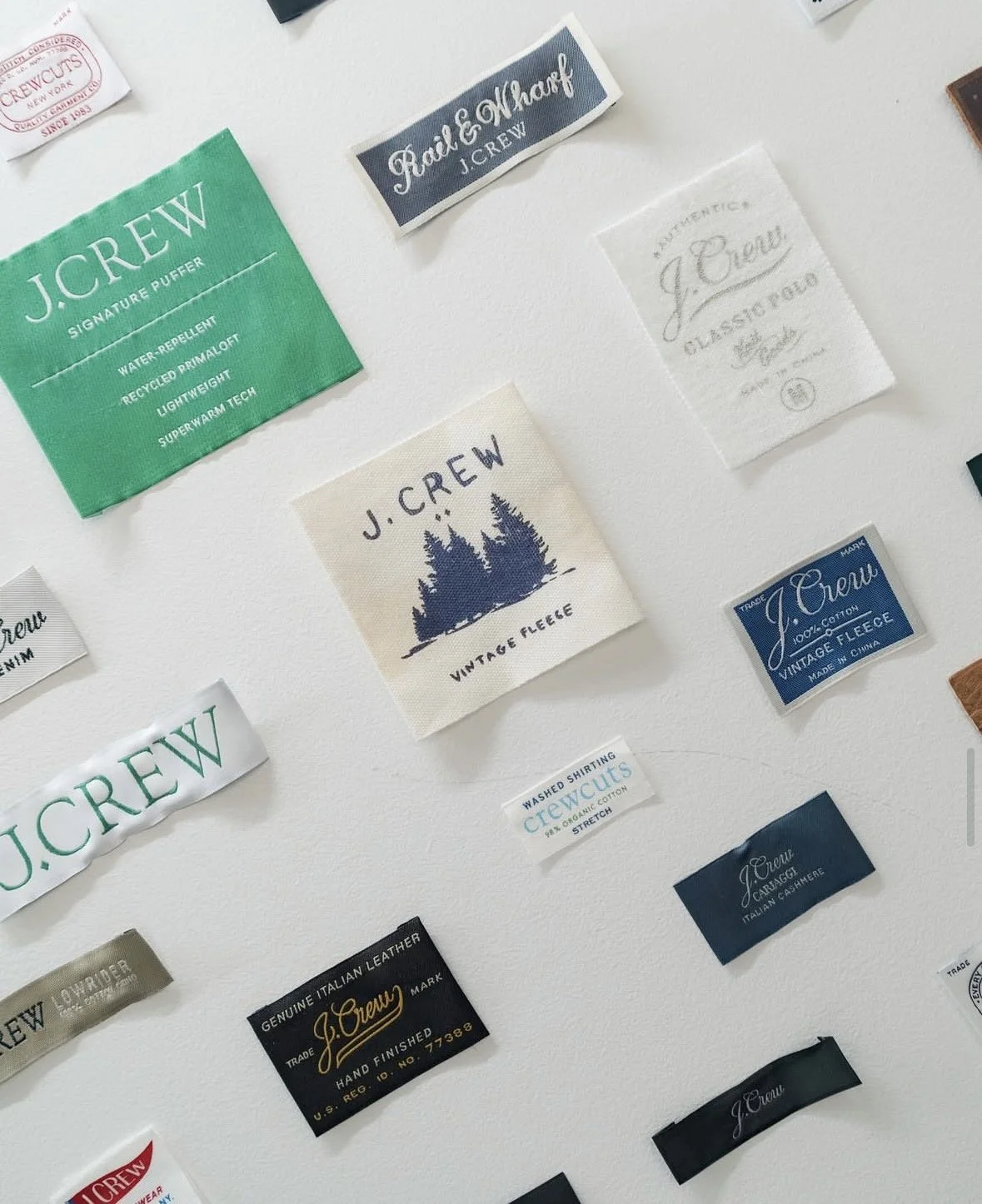 Collection of fabric care labels and tags from J.Crew, featuring various designs, colors, and fonts, including green, black, blue, white, and beige tags with different texts and logos.