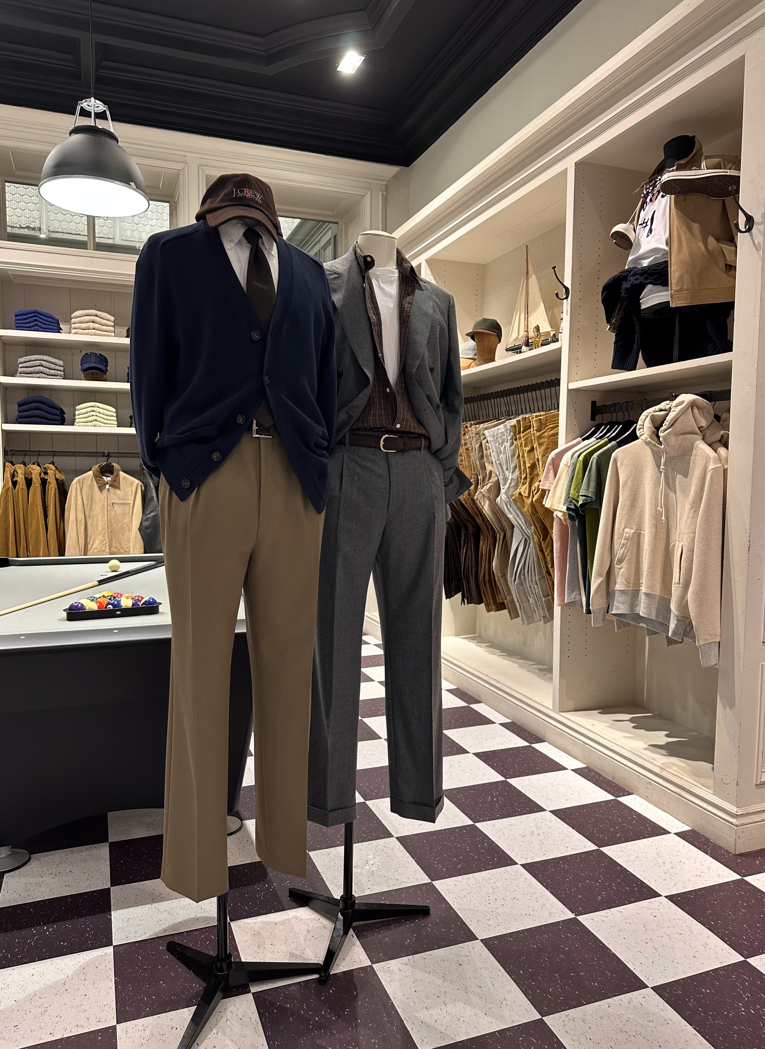 Mannequins dressed in suits and casual wear inside a clothing store with shelves of folded clothes and hanging garments.