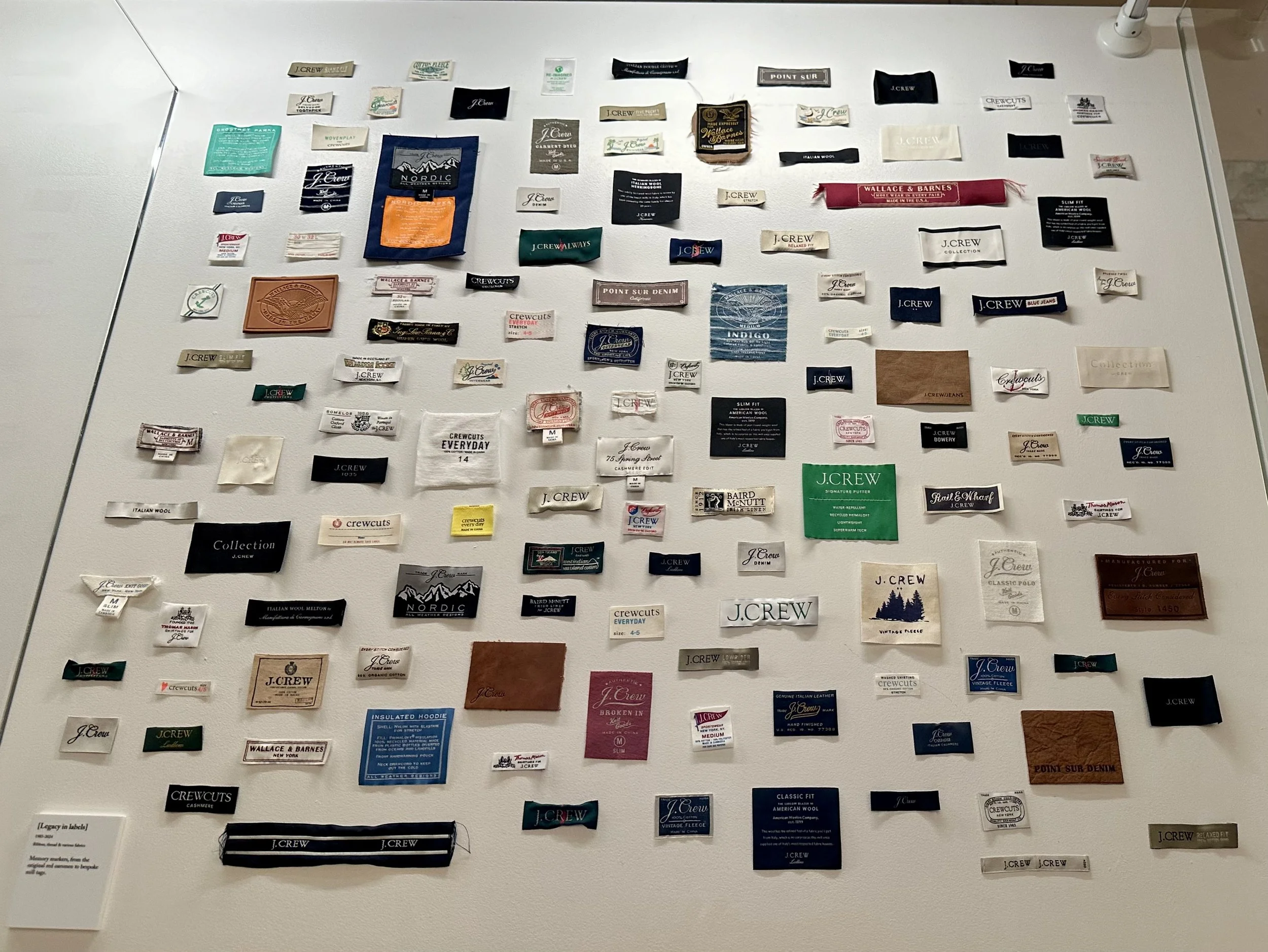 A wall covered with numerous labels, tags, and fabric swatches from J.Crew clothing items.