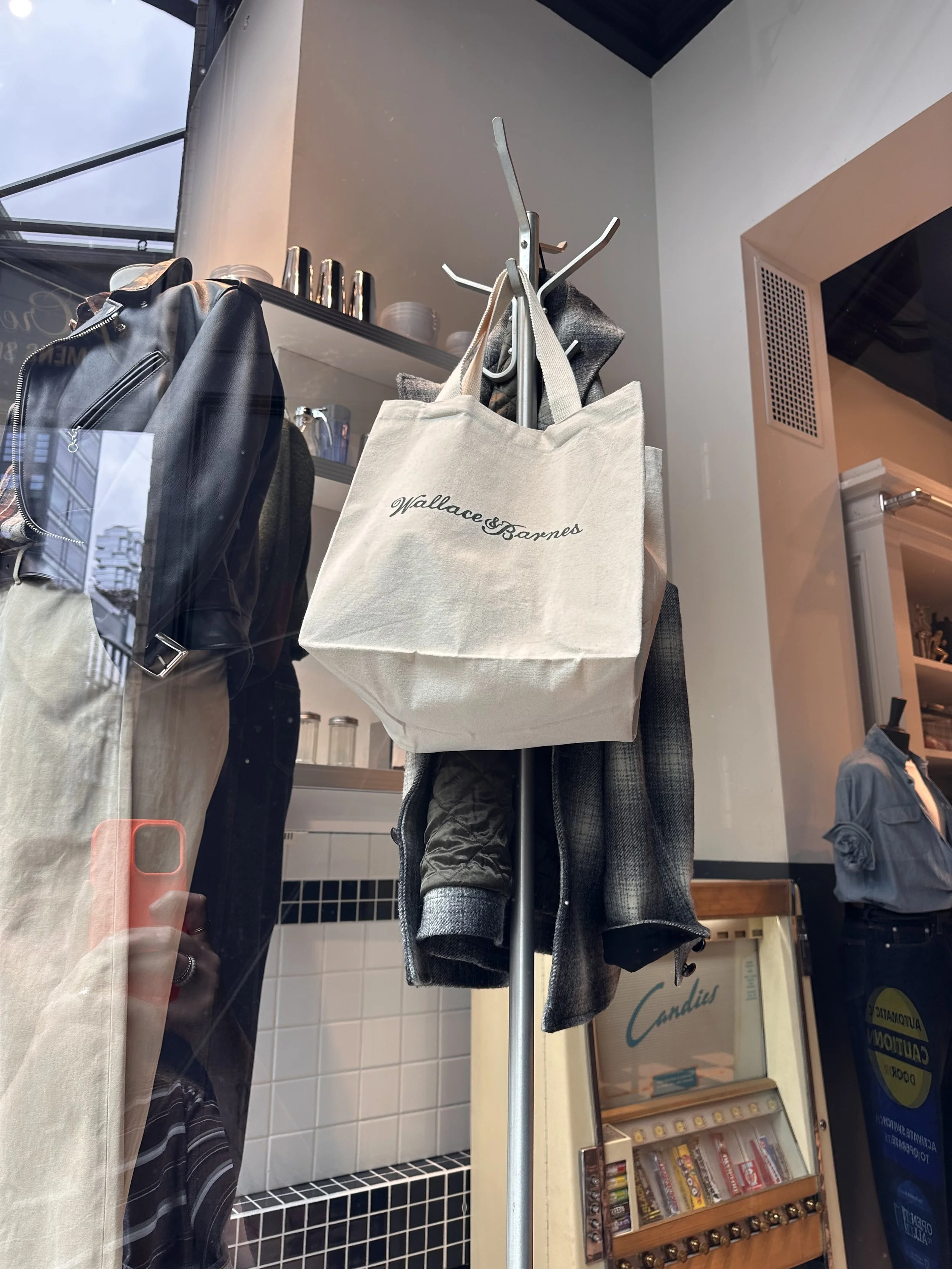 A beige Wallace & Barnes tote bag hanging on a coat stand inside a store.
