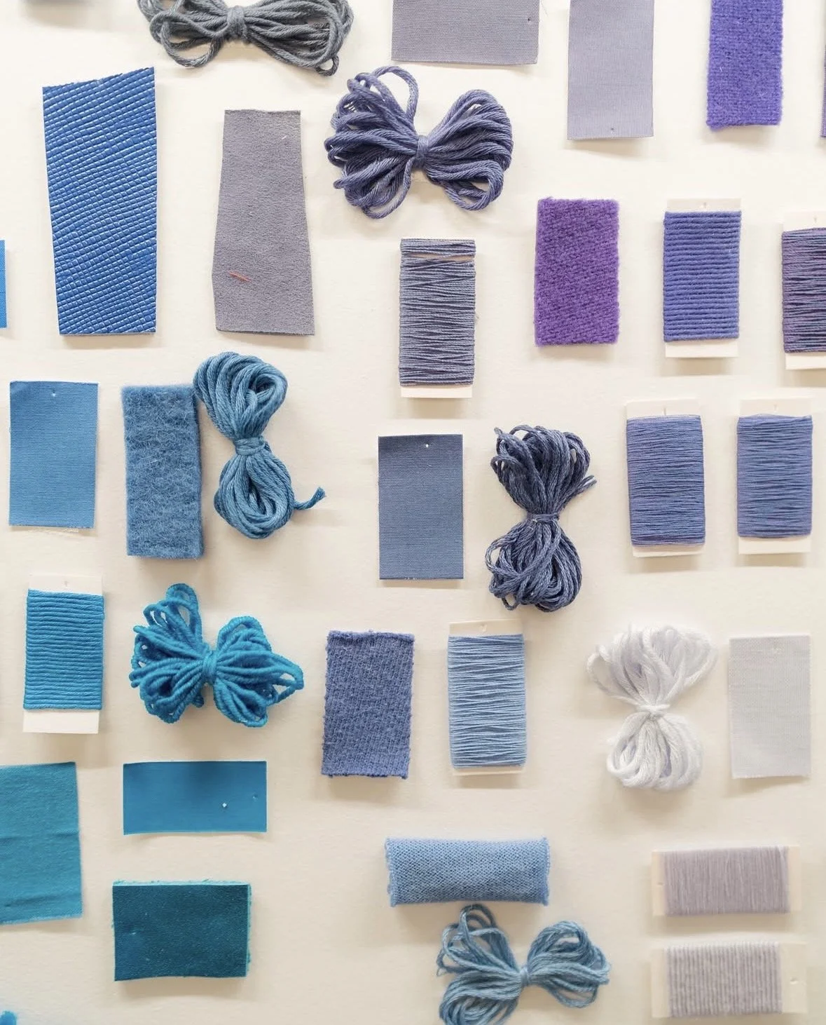 Various swatches of blue, purple, and white fabric and yarn samples arranged on a white background.