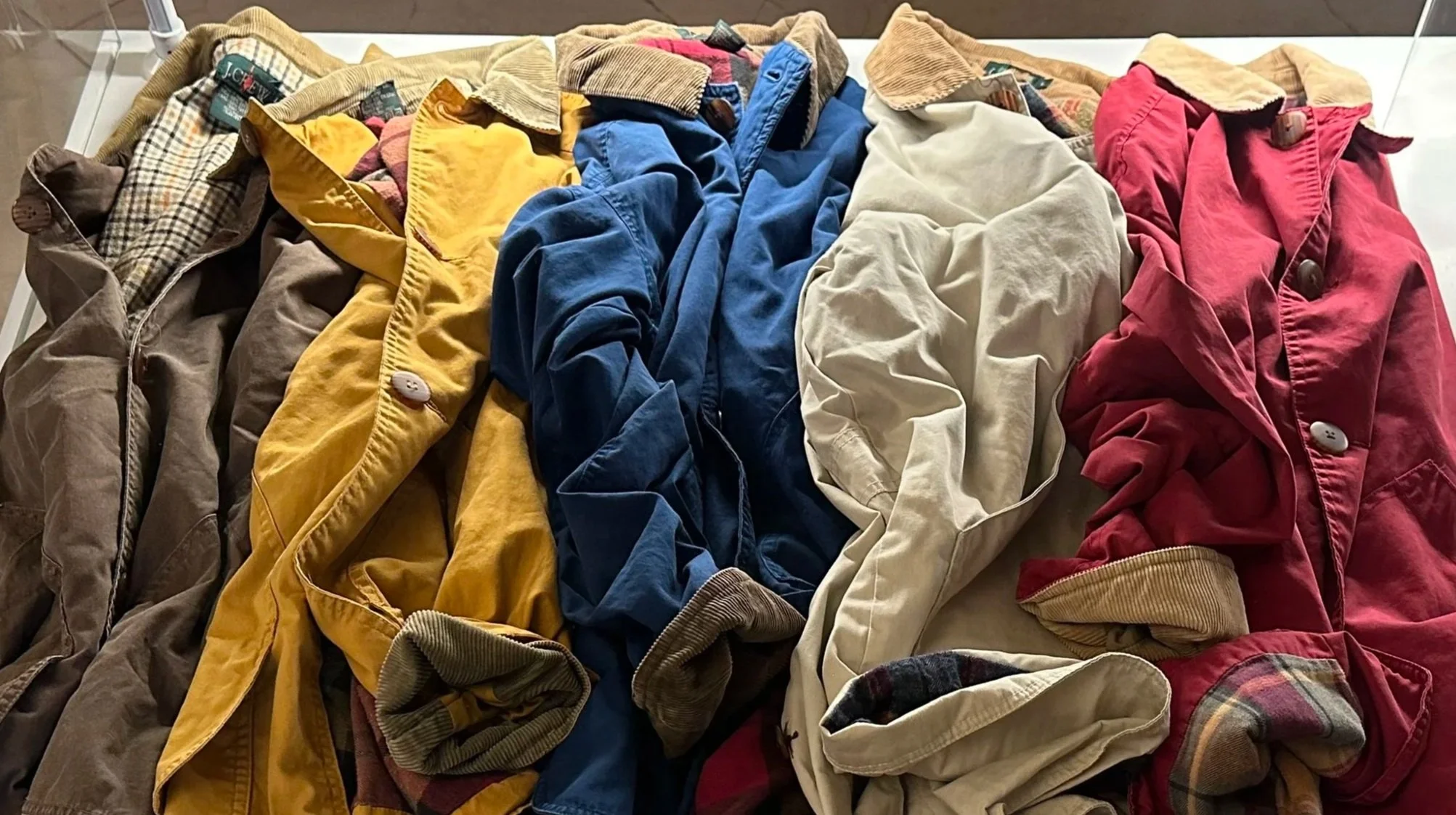 A display case with old, wrinkled, and disorganized jackets in various colors, including brown, yellow, blue, beige, and red.