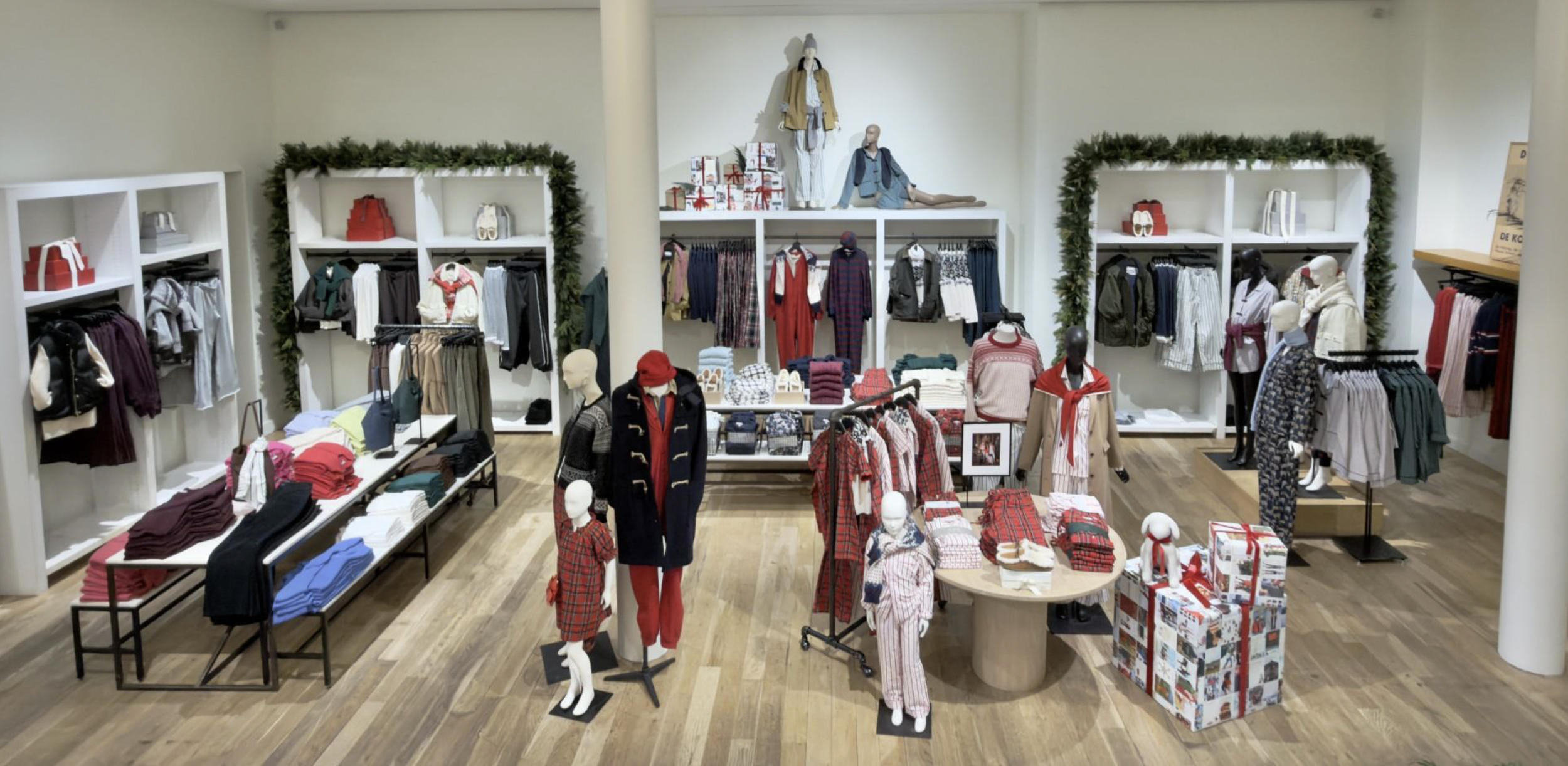 Clothing store display with mannequins dressed in winter outfits, shelves with folded clothes, and christmas-themed decorations.
