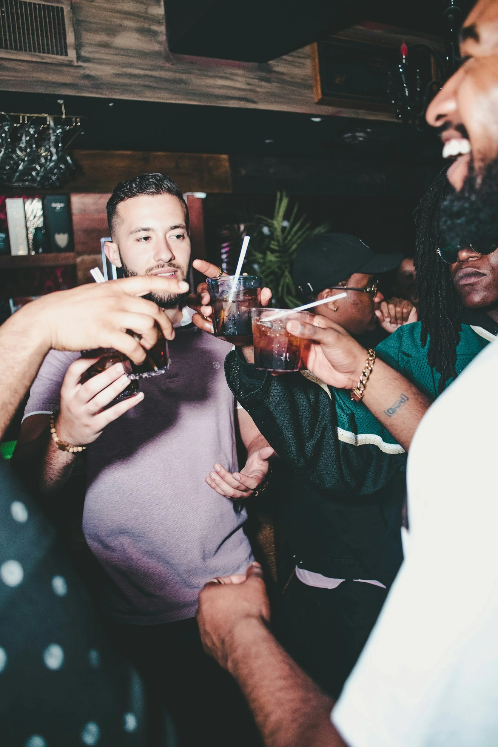 Group of friends clinking glasses with dark beverages in a dimly lit bar.
