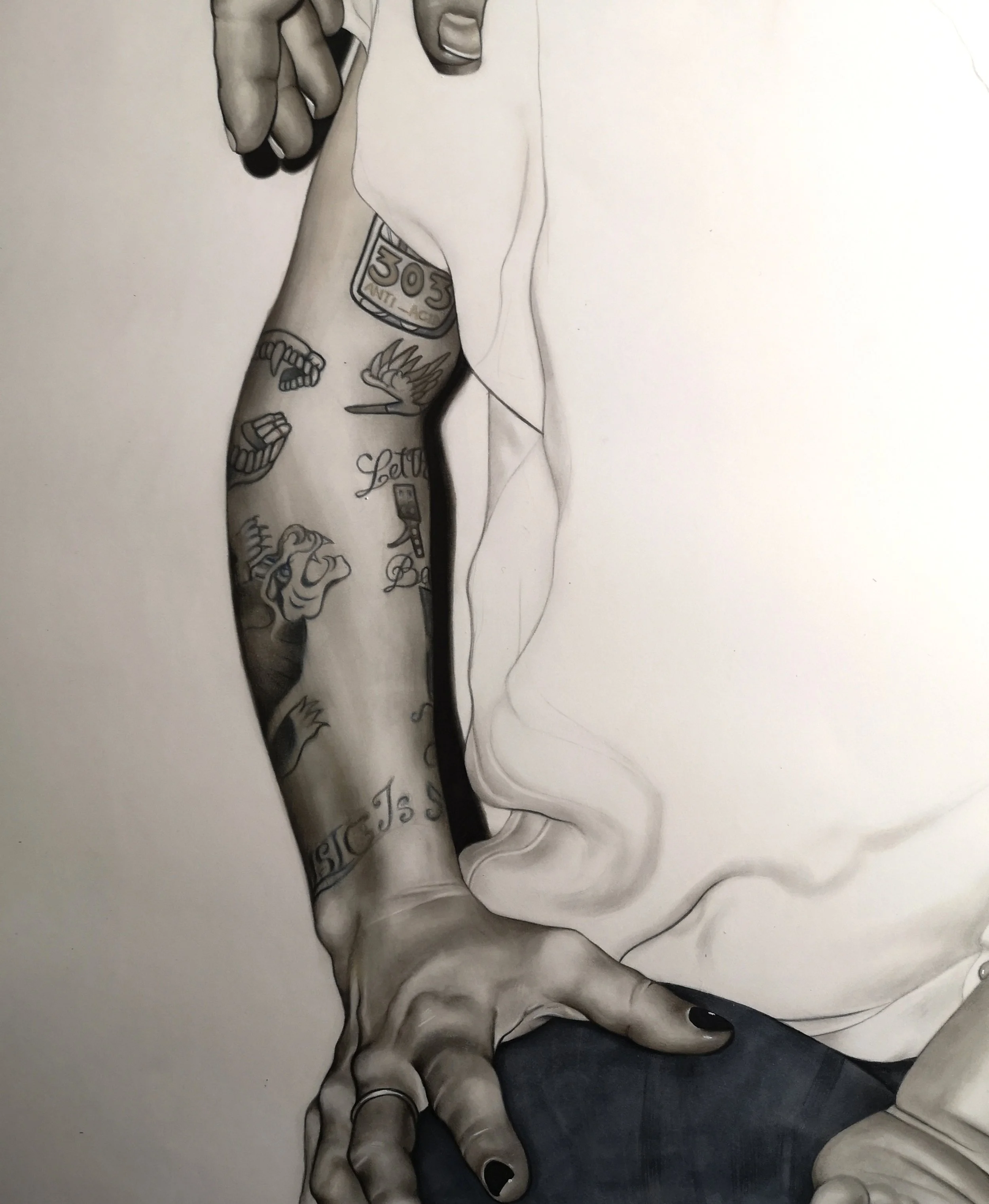 Close-up of a person's arm with tattoos, holding a cigarette, with a hand resting on a knee with dark nail polish, partially covered by a white shirt