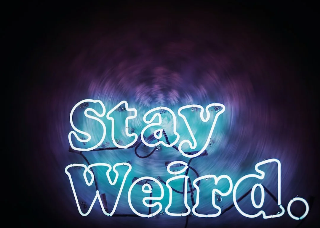 Blue neon sign that says "stay weird"